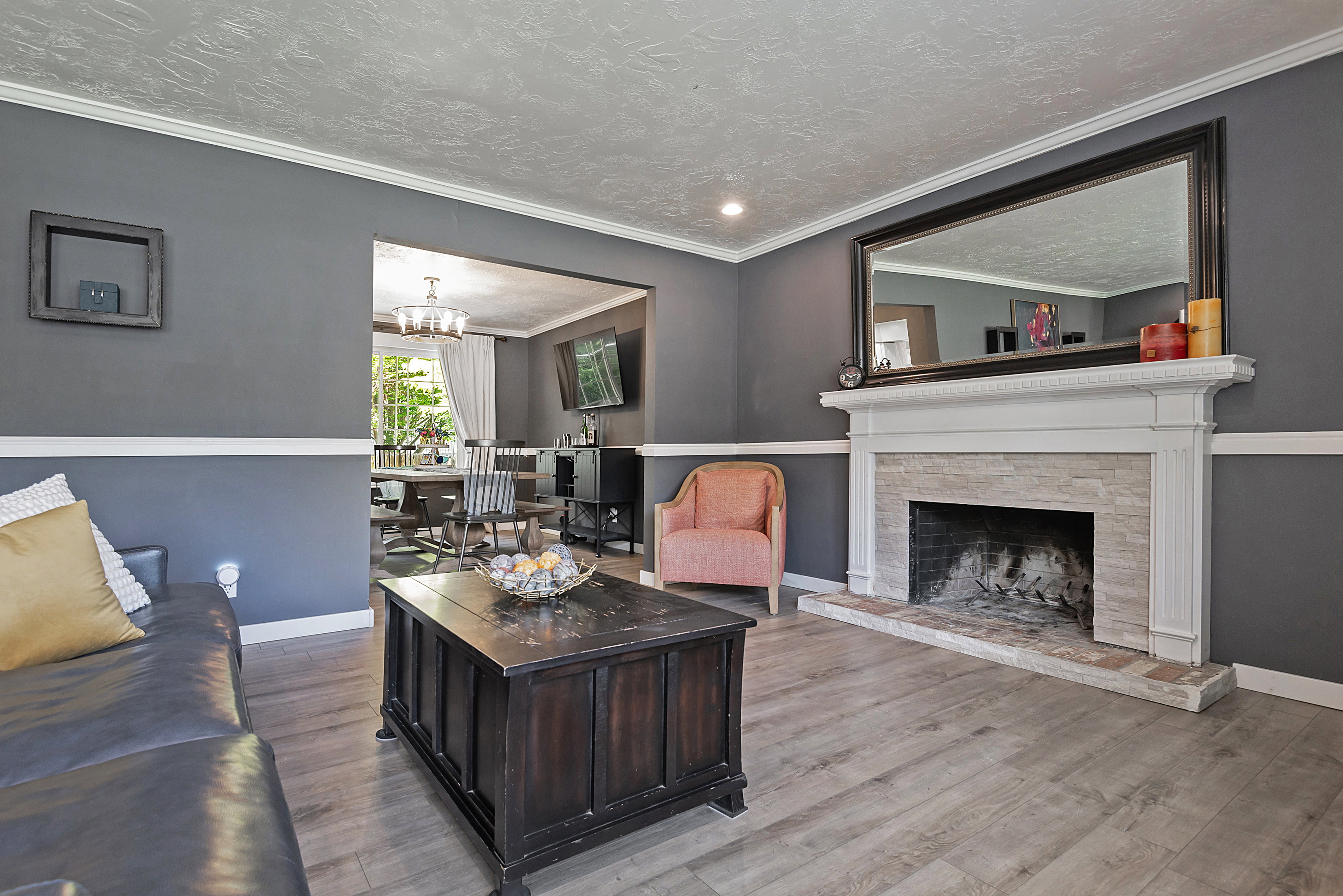 Living area featuring a white mantel fireplace with stone surround, wood-finish flooring, two-tone wall treatment, crown molding, and recessed lighting