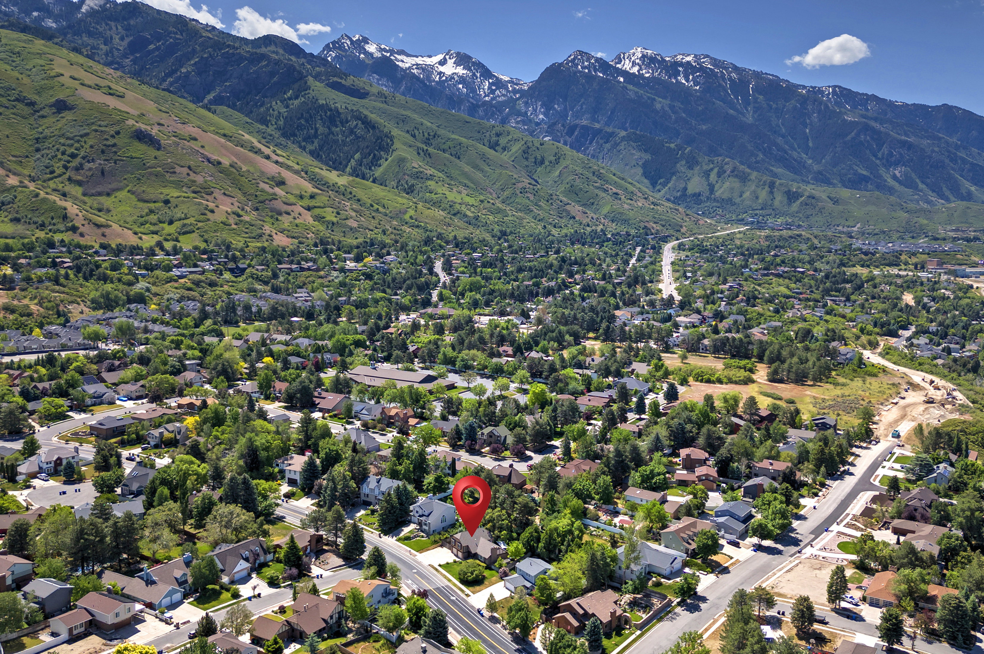 Aerial perspective showcasing a residential neighborhood with tree-lined streets, against a backdrop of green hills and snow-capped mountains