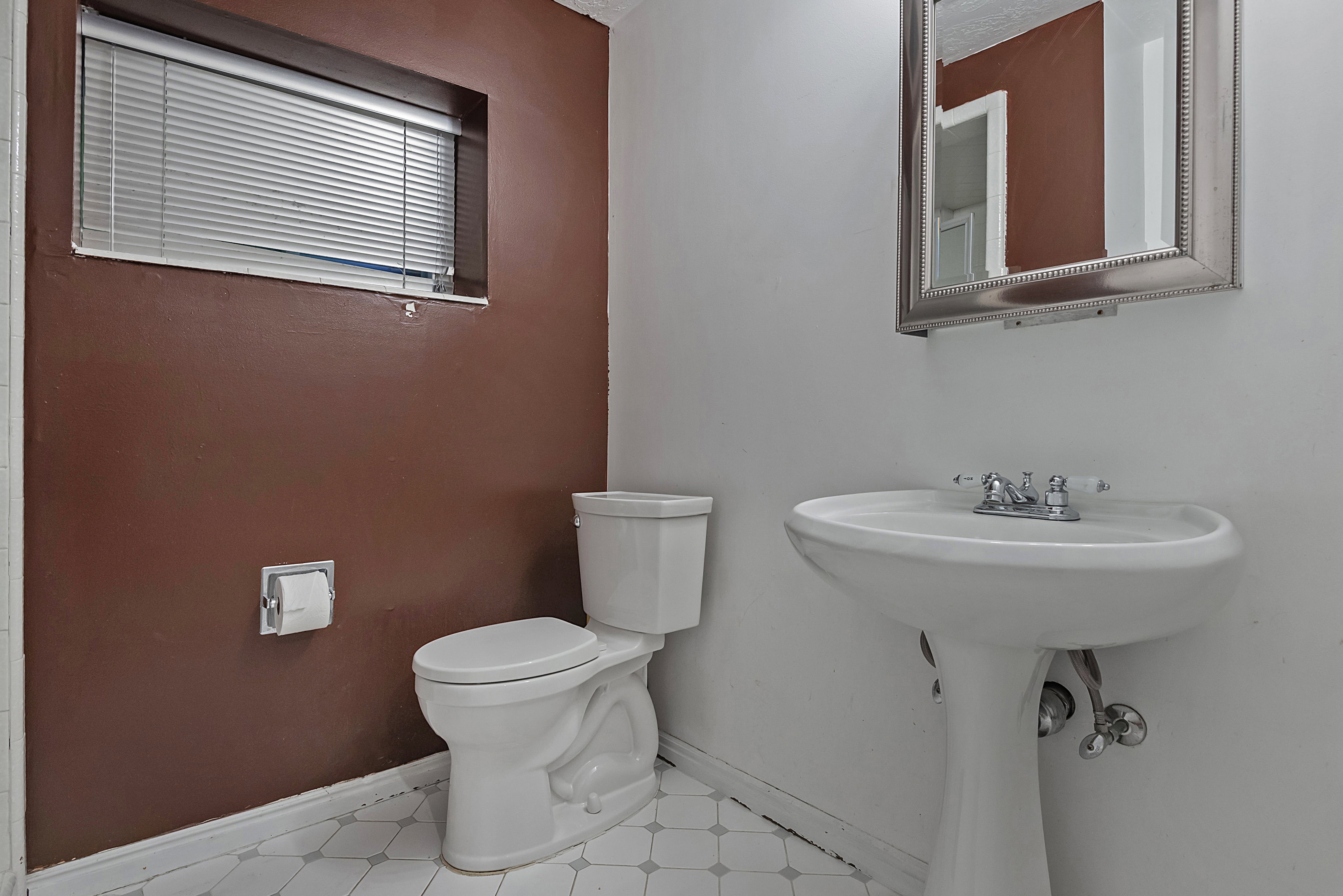 Bathroom featuring a white pedestal sink with chrome fixtures, a white toilet, and a window with blinds