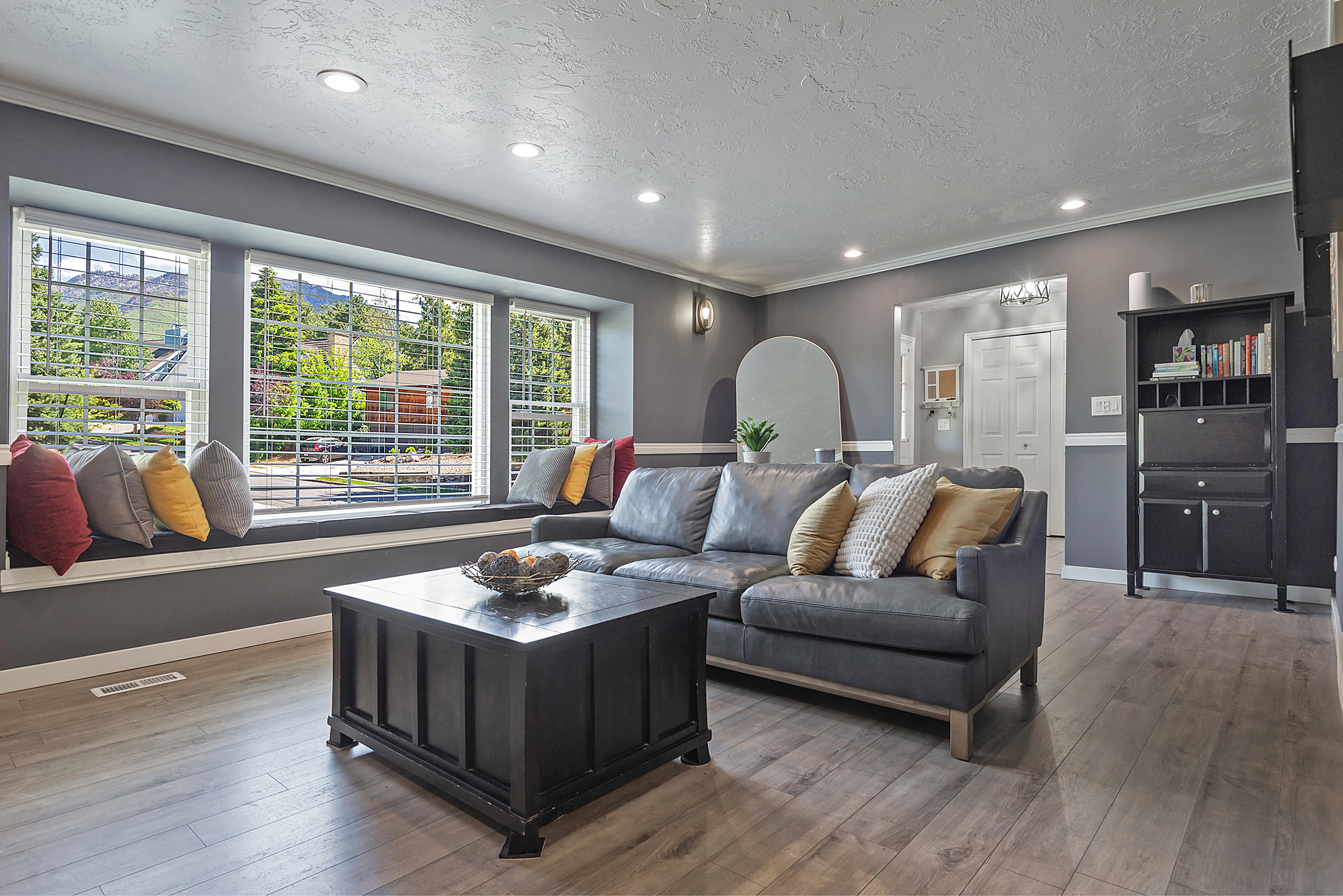 Spacious living area featuring a wide window seat with multiple windows, wood-finish flooring, recessed lighting, crown molding, and a two-tone wall treatment