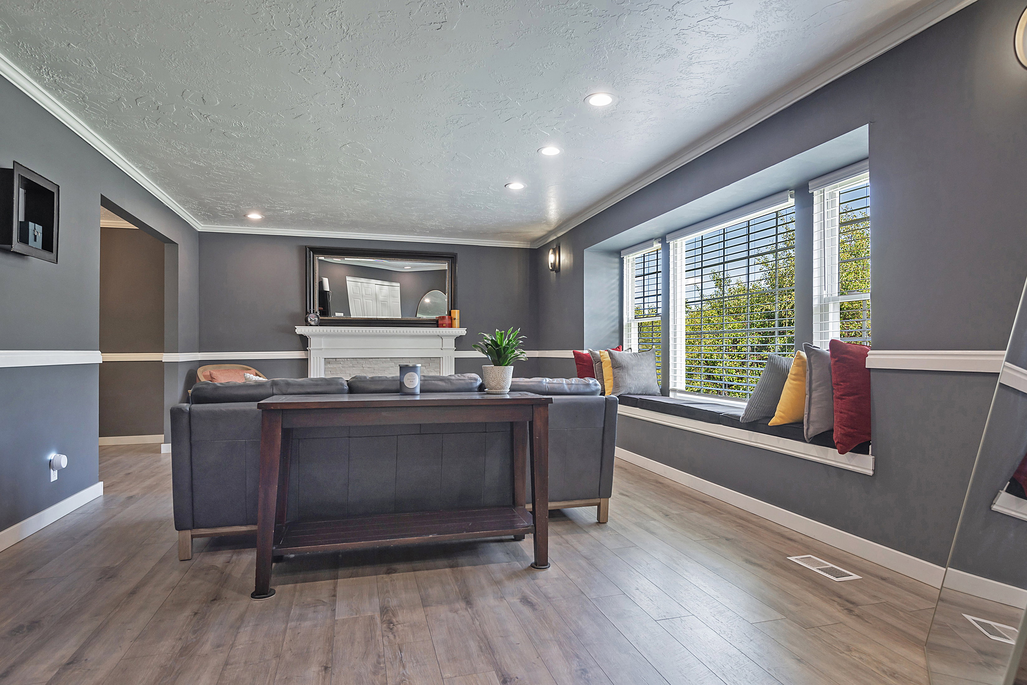 Living area featuring wood-finish flooring, a built-in window bench, a fireplace with a white mantel, recessed lighting, and crown molding