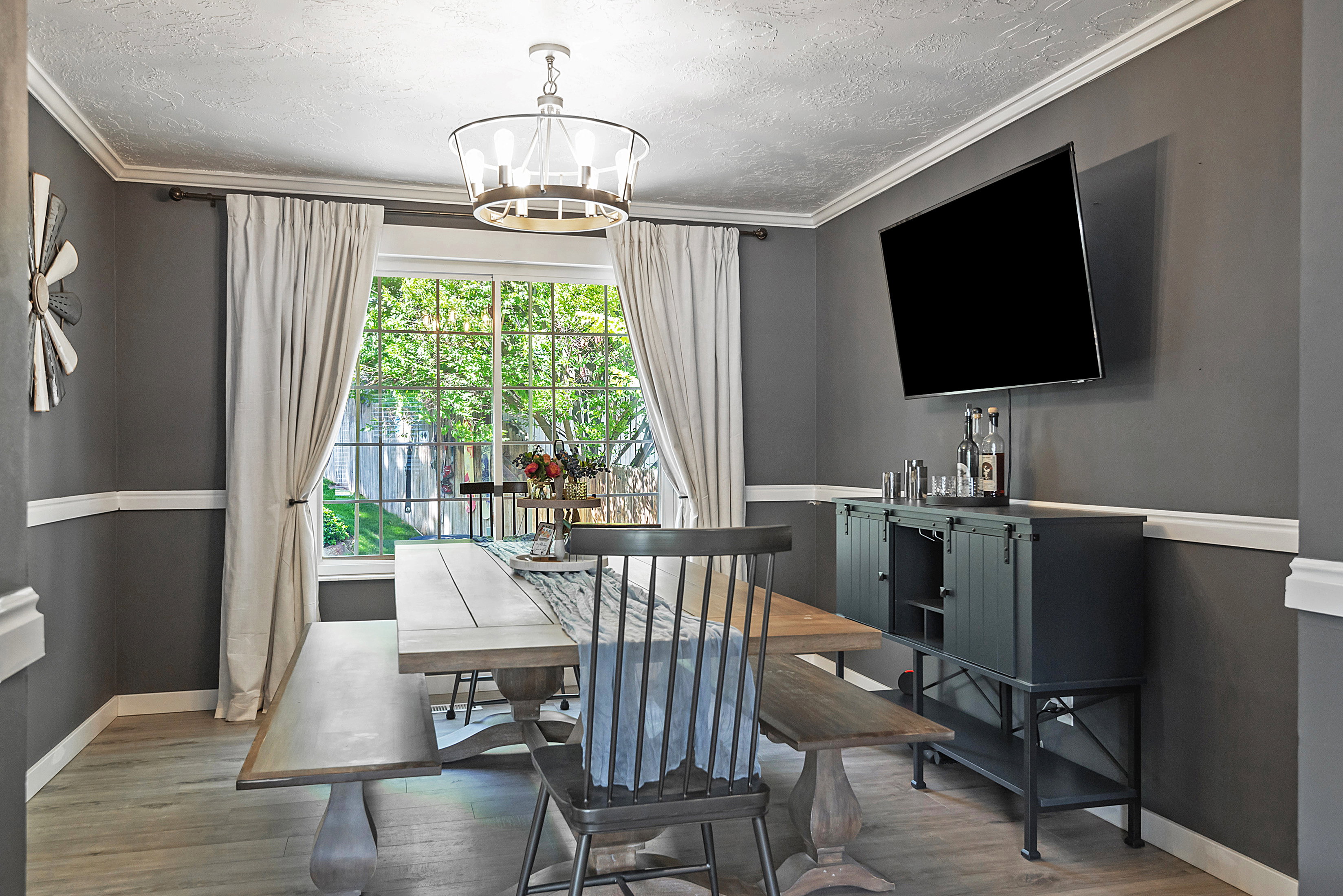 Dining space with wood-finish flooring, featuring a large window with white drapes, and a contemporary chandelier