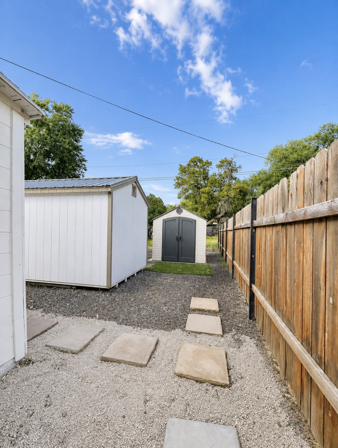 Backyard area featuring two storage sheds with metal roofs, a wooden privacy fence, and a gravel ground cover with stepping stones