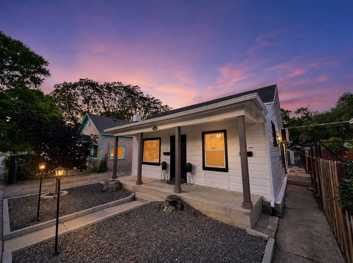 White siding exterior with dark trim accents, a covered front porch, and a gravel front yard with path lighting