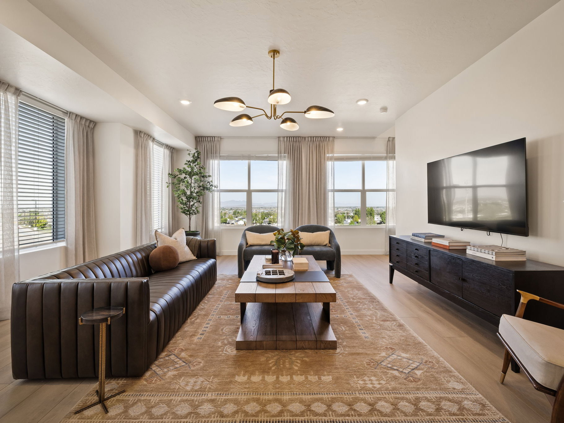 Spacious living area featuring light wood-finish flooring, a contemporary chandelier, recessed lighting, and multiple windows with blinds and sheer drapes