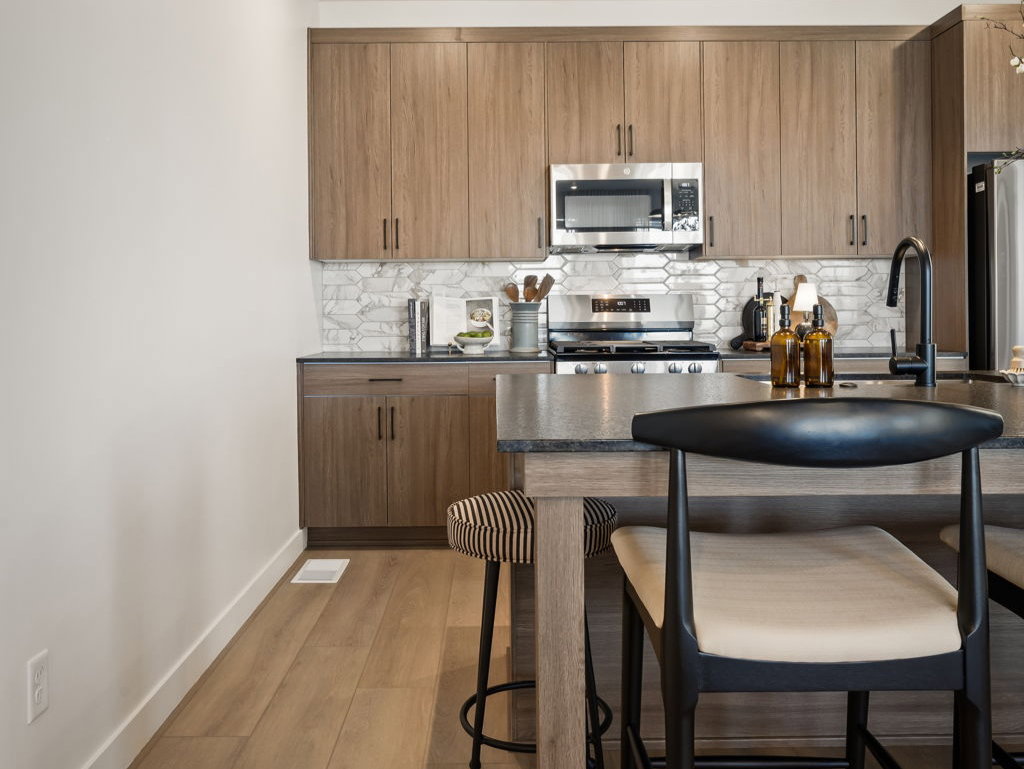 Kitchen featuring wood-finish flooring, full-height cabinetry, stainless steel microwave, and an island with a dark countertop