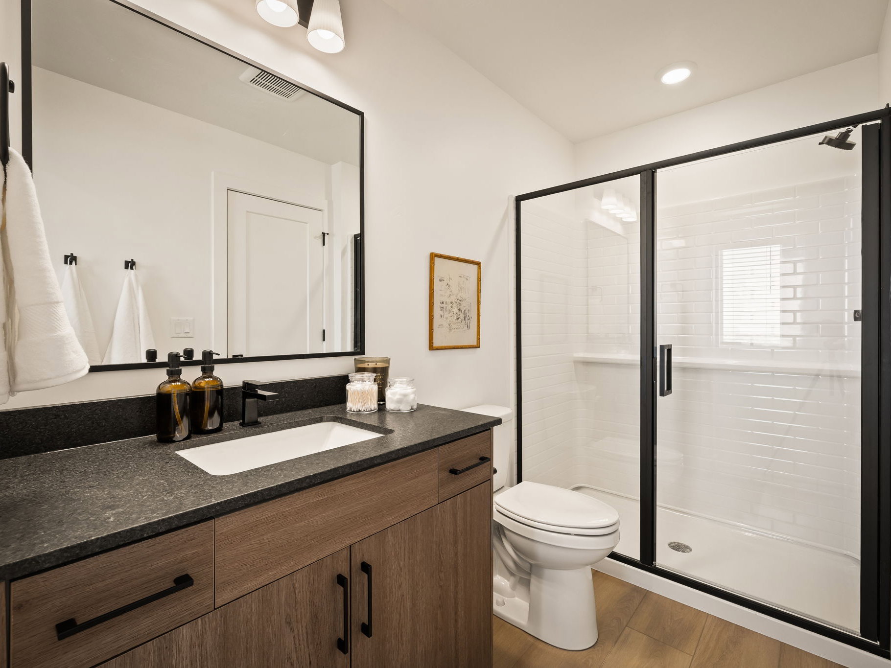 Contemporary bathroom featuring a dark stone countertop, wood-finish vanity with dark hardware, and a framed mirror
