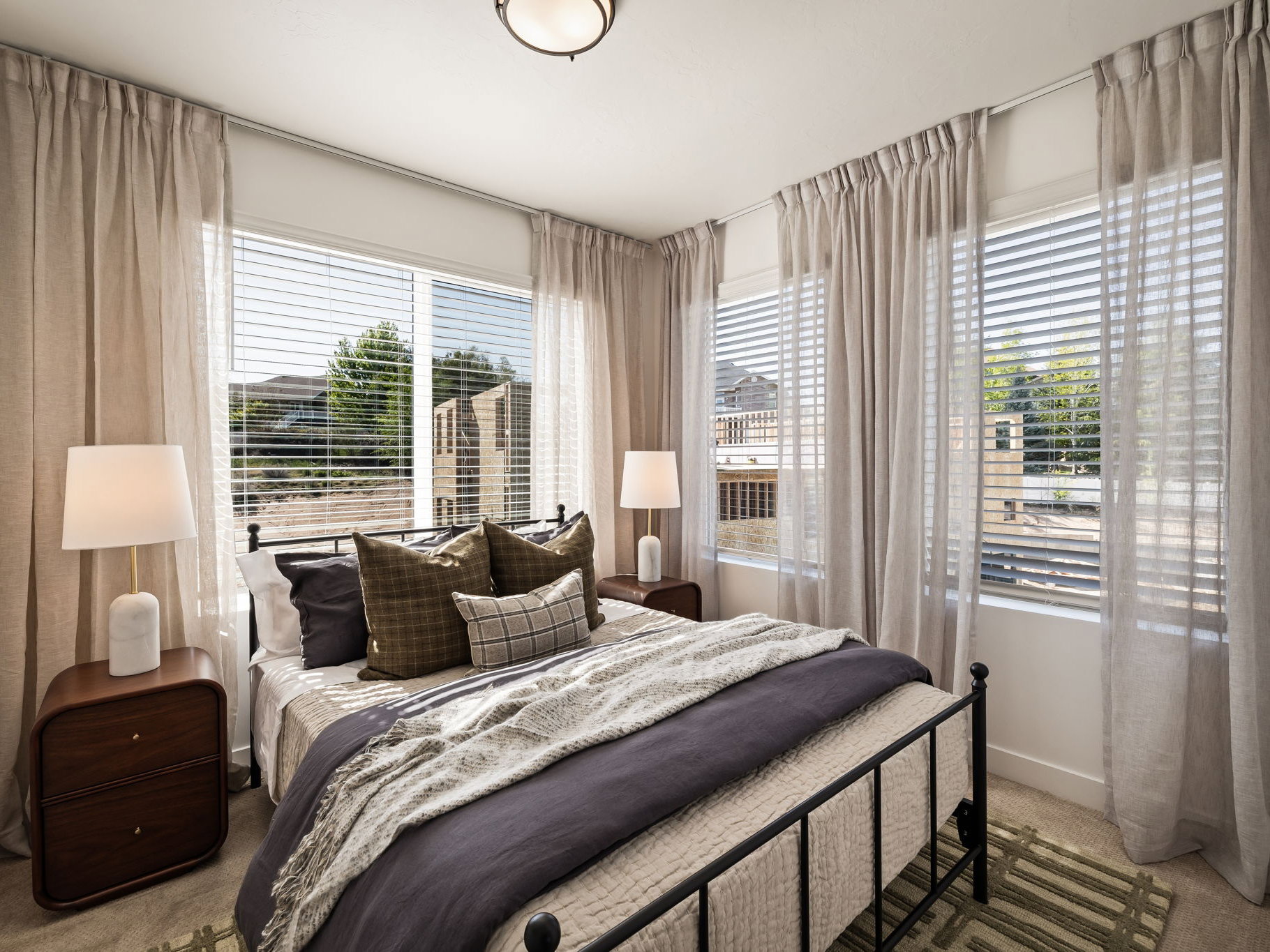 Bedroom featuring a multi-pane window with blinds, light-toned drapery, a ceiling-mounted light fixture, and neutral carpet flooring