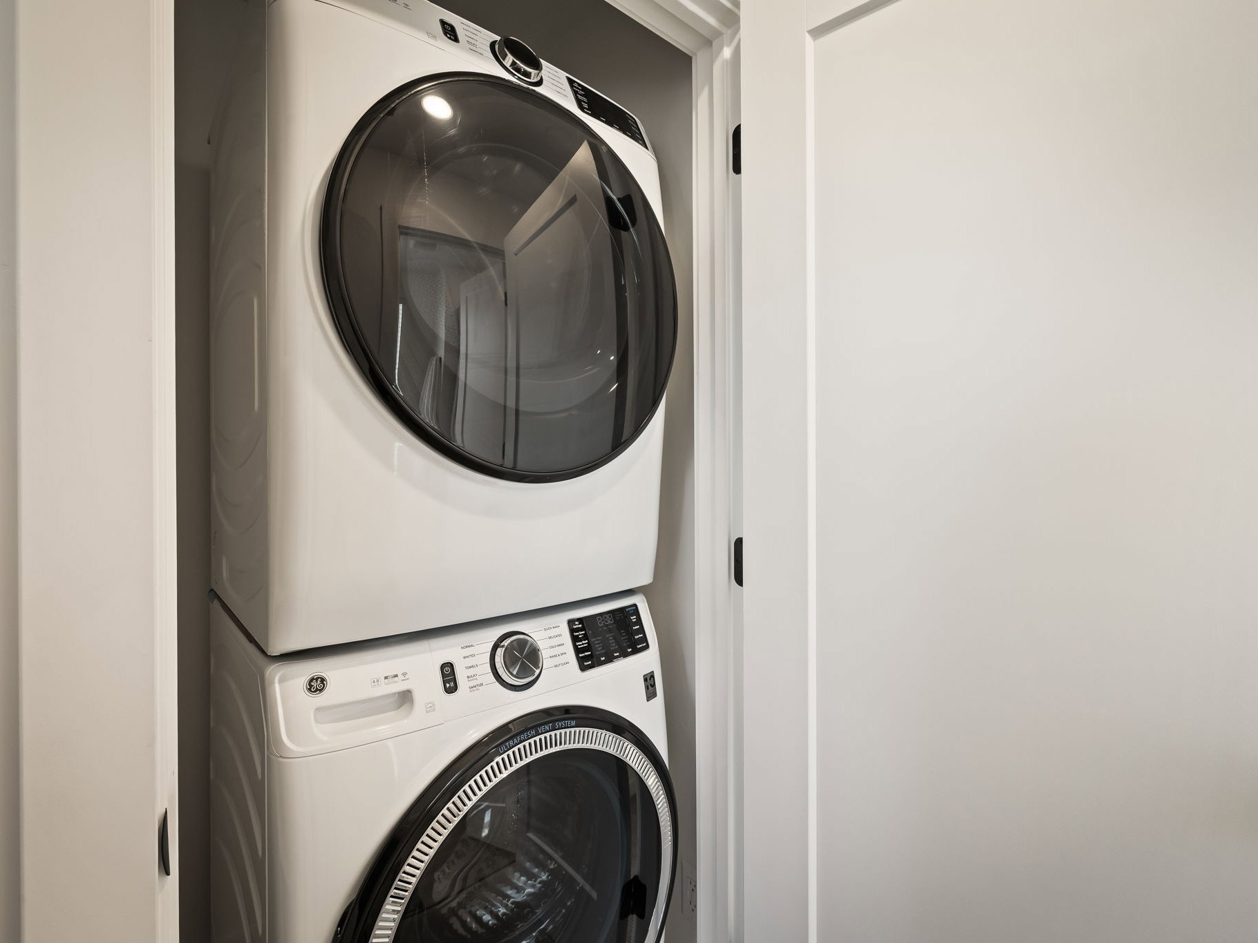 Dedicated laundry closet featuring a stacked white front-load washer and dryer set