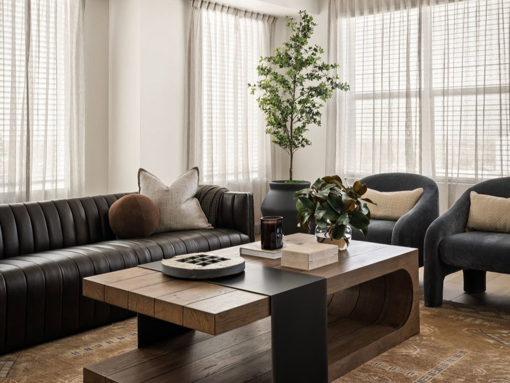 Spacious living area featuring a multi-paneled window array with privacy blinds, a modern ceiling light fixture, a dark wood-finish coffee table with black accent elements, and an area rug with a patterned design