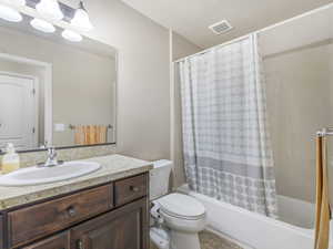 Bathroom featuring a wood-finish vanity with an integrated sink, a speckled countertop, an elongated toilet, a shower-over-tub combination, and a full-width wall mirror