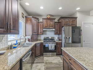 Kitchen featuring rich wood cabinetry, stone countertops, stainless steel appliances, and a mosaic tile backsplash