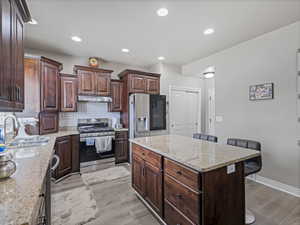 Kitchen featuring a central island with a stone countertop, dark wood-finish cabinetry, stainless steel appliances, recessed lighting, and wood-finish flooring