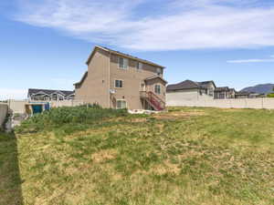 Expansive backyard featuring a large grass area, a two-story residence with a tan stucco exterior, and a red outdoor staircase