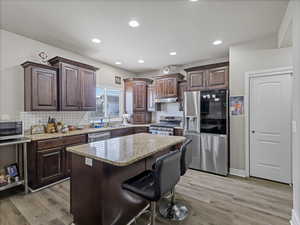 Kitchen featuring a central island with granite countertop, dark wood cabinetry, stainless steel appliances, and wood-finish flooring