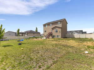 Expansive backyard featuring a stucco exterior, multiple windows, an exterior staircase, and perimeter fencing