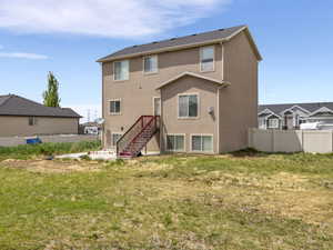 Rear exterior featuring a stucco facade, multiple windows providing natural light, a dark shingle roof, and an exterior staircase with red stringers and wood treads