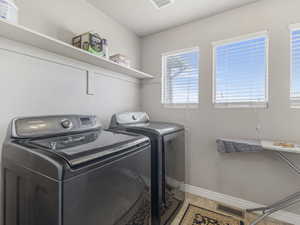 Dedicated laundry area featuring a built-in shelf, two windows with blinds, and durable tile flooring