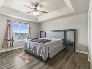 Bedroom featuring wood-finish flooring, a tray ceiling, and a ceiling fan with integrated lighting