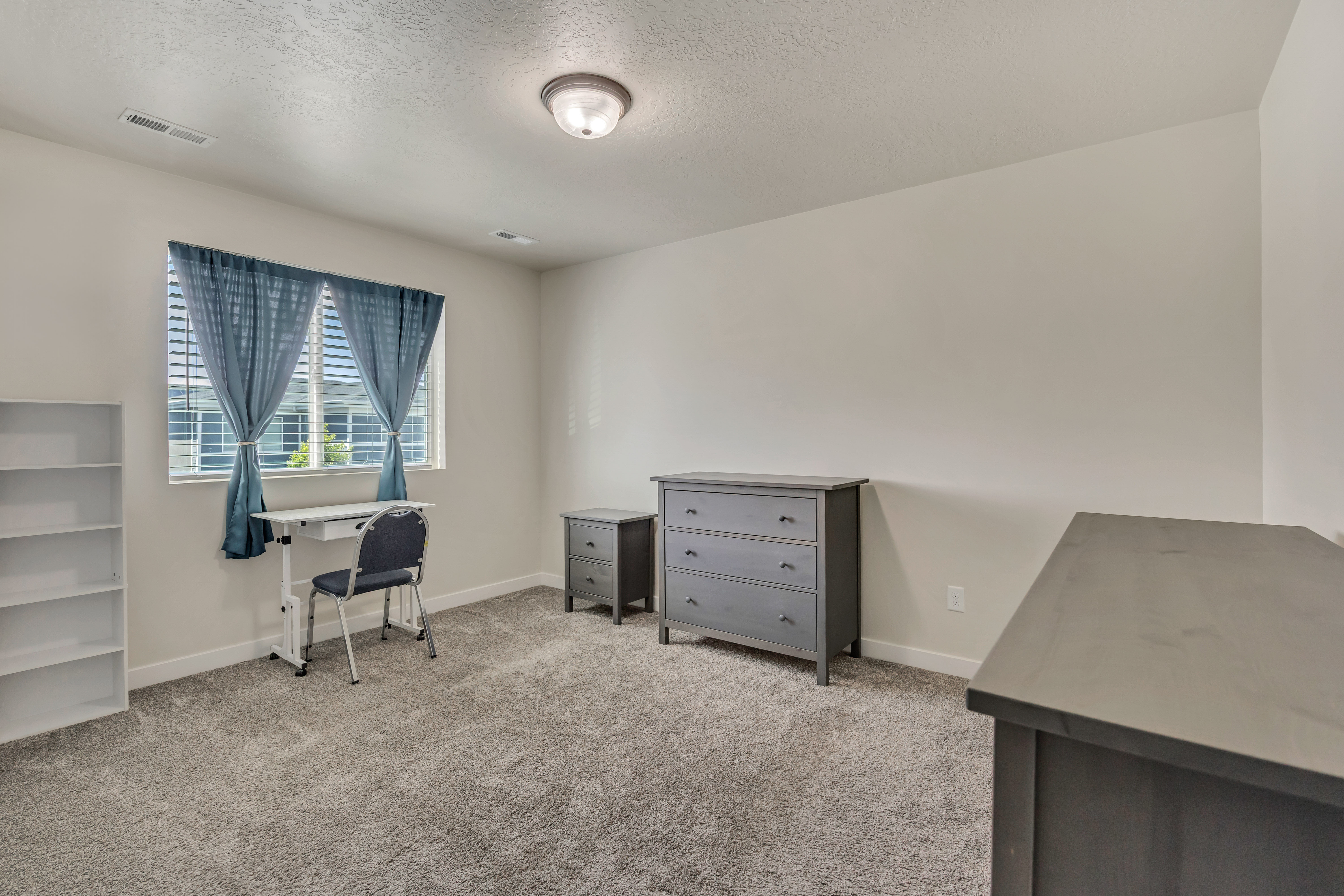 Carpeted room with a ceiling light fixture, white walls, and a window featuring blinds