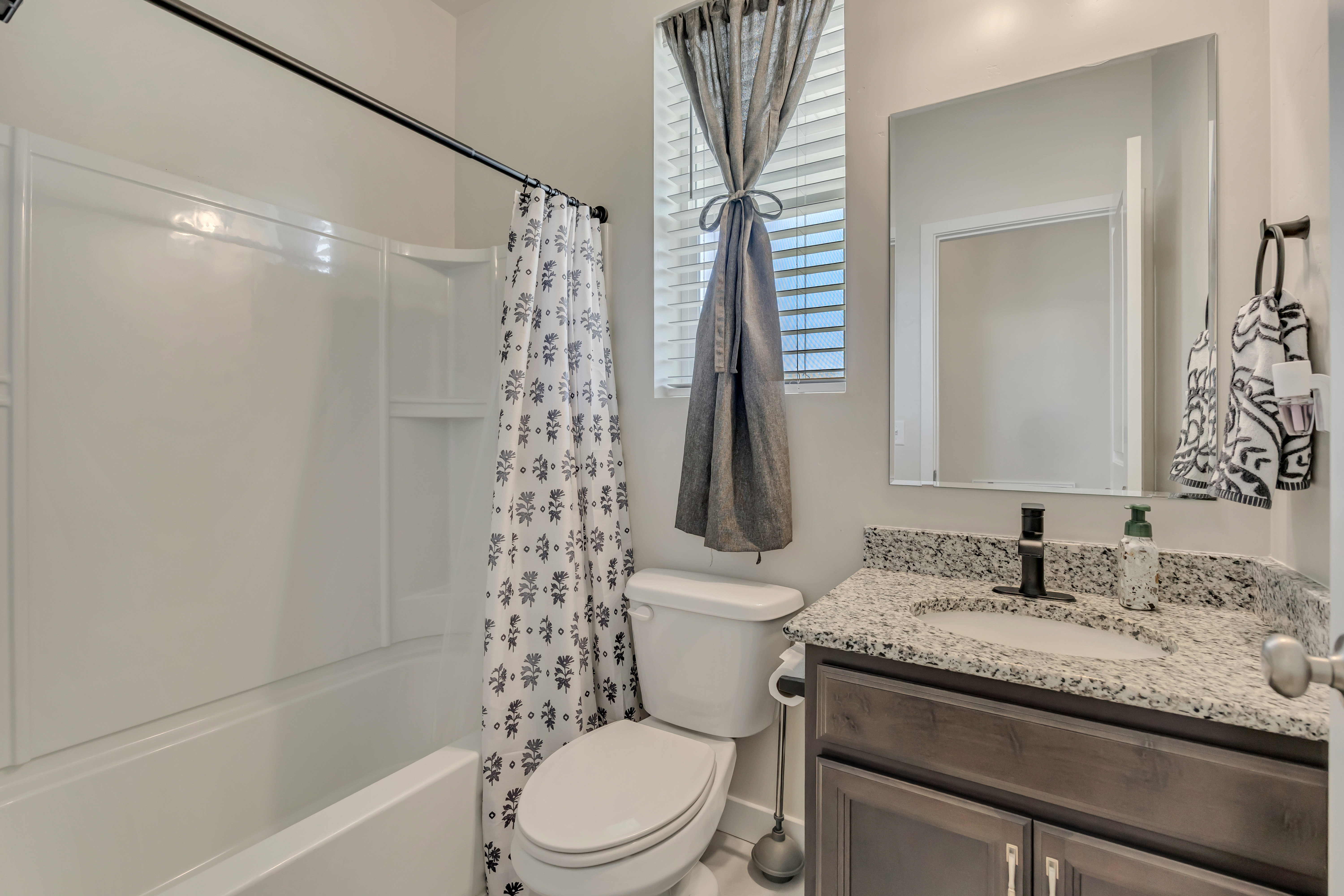 Bathroom featuring a white tub/shower combination, dark wood-finish vanity with a granite-style countertop, undermount sink, and matte black faucet