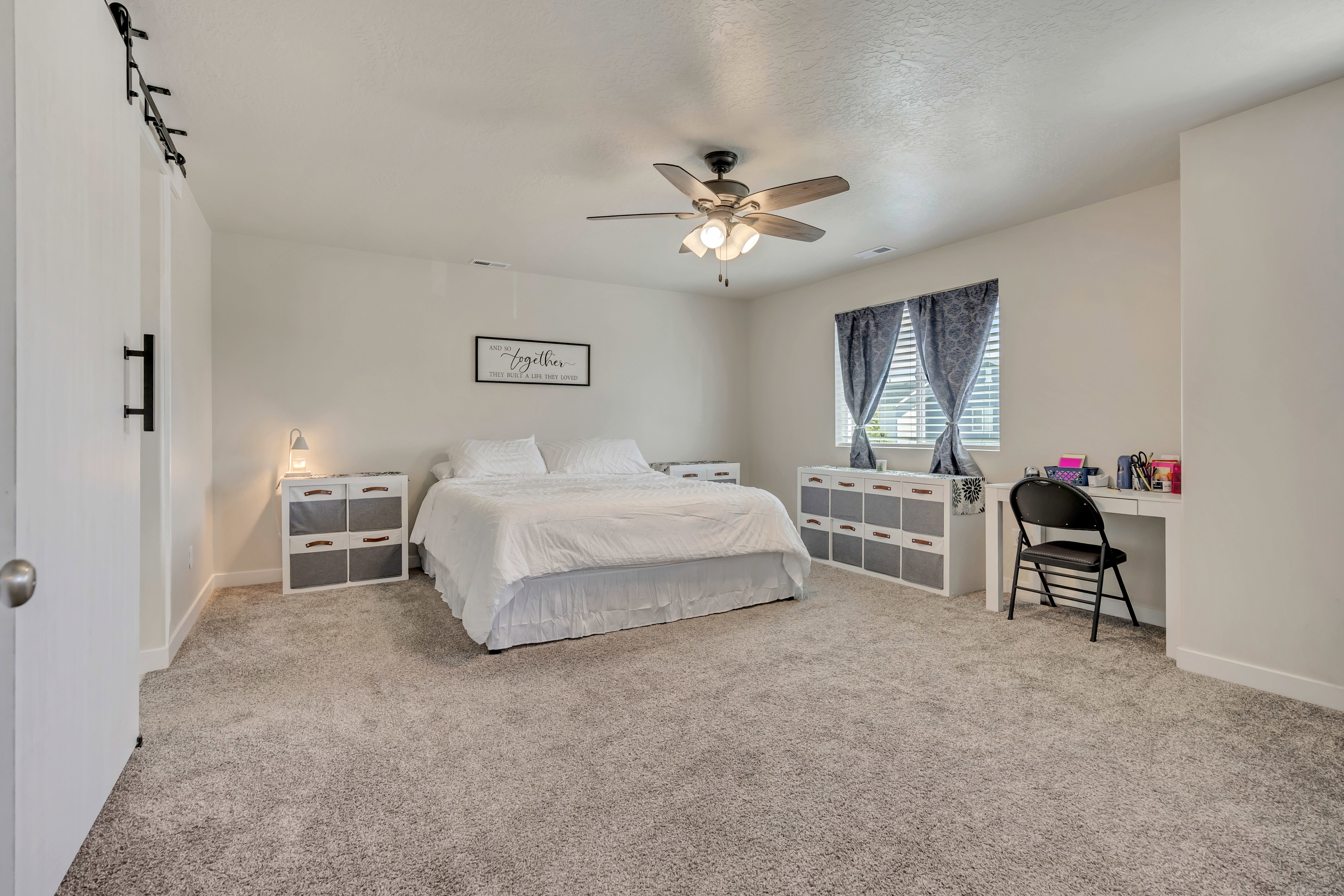 Spacious bedroom featuring plush gray carpeting, a multi-speed ceiling fan with integrated lighting, and white walls