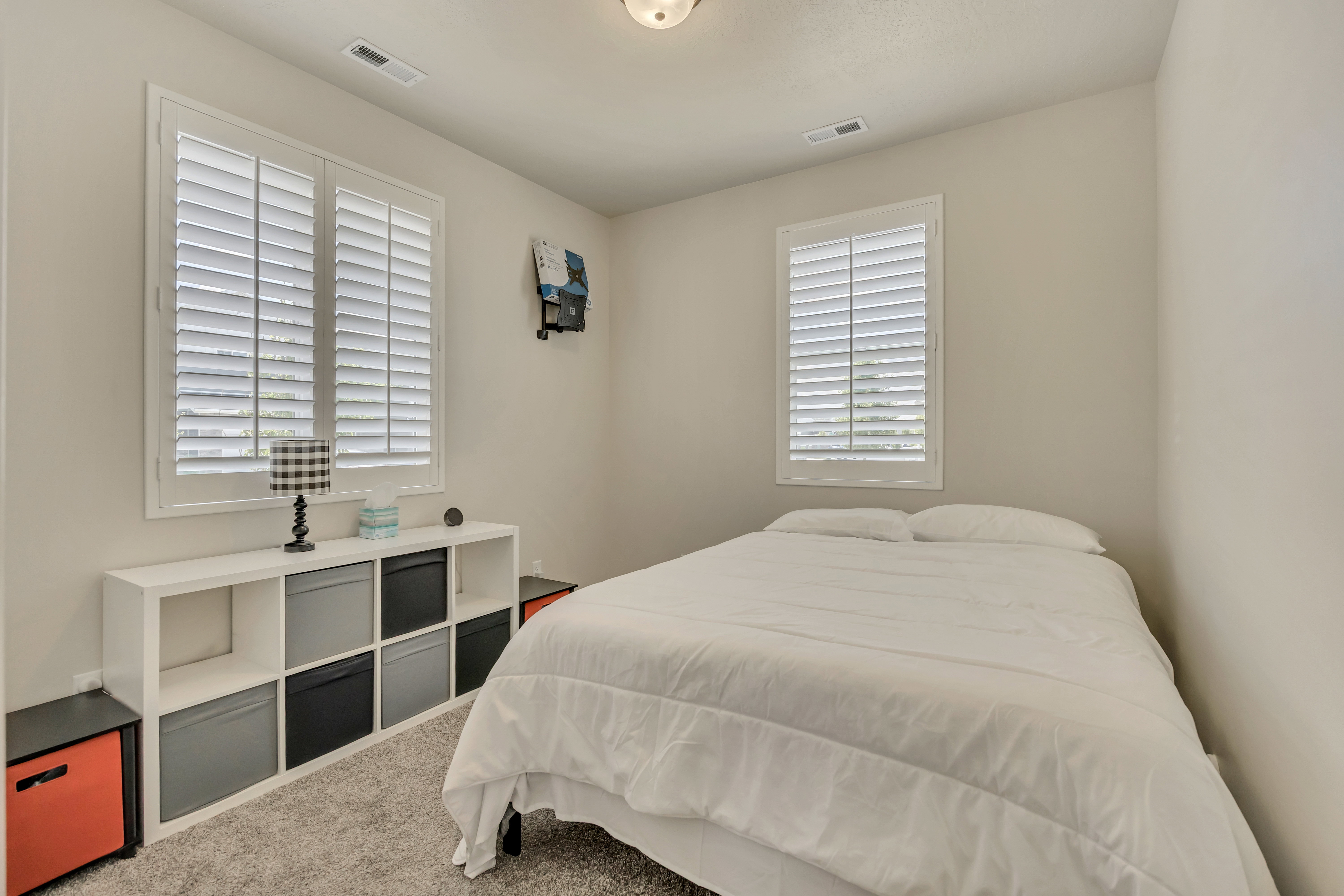 Carpeted room featuring two windows with white plantation shutters, neutral wall paint, and a ceiling-mounted light fixture