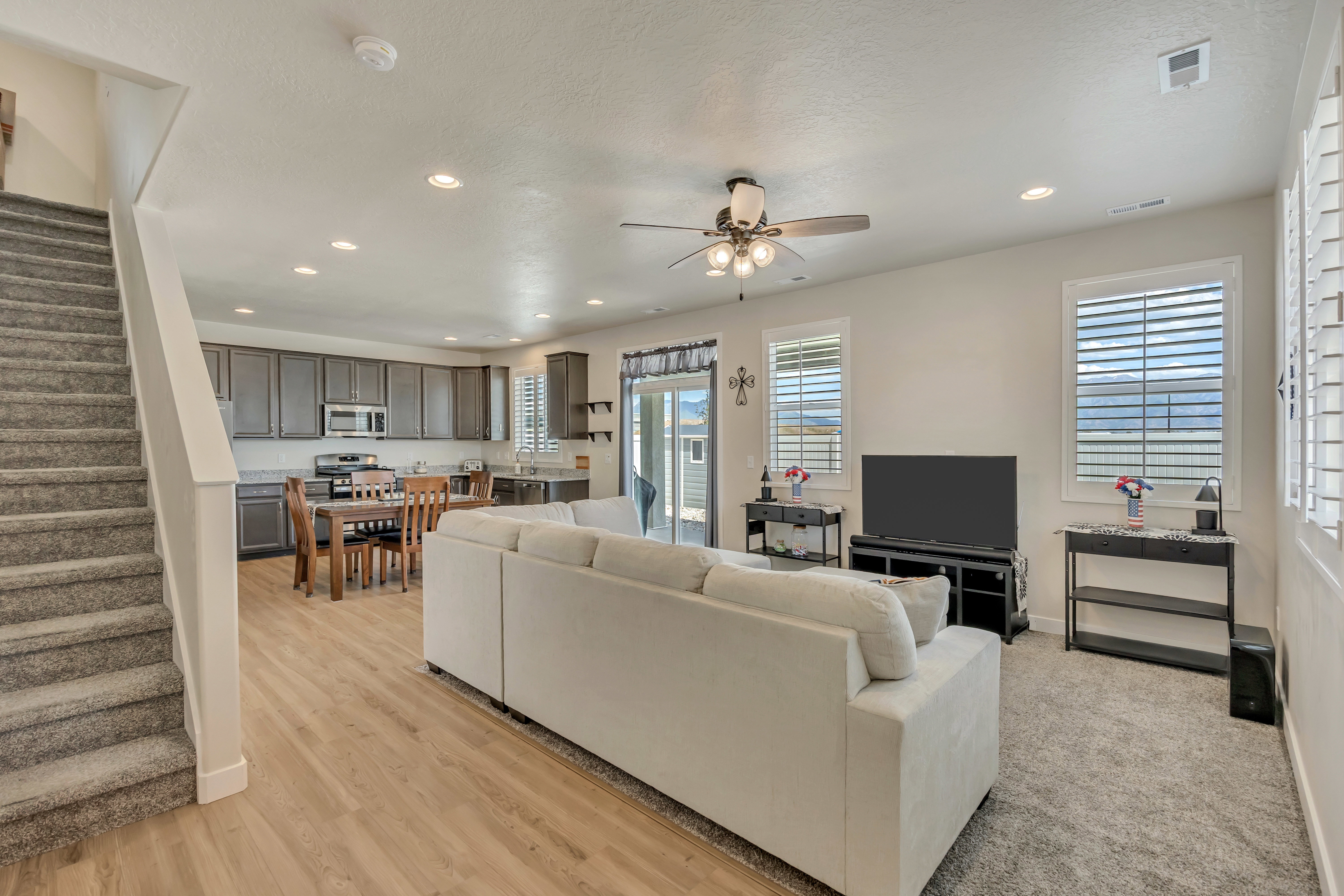 Open-concept living space featuring wood-finish flooring, recessed lighting, a ceiling fan, and plantation shutters