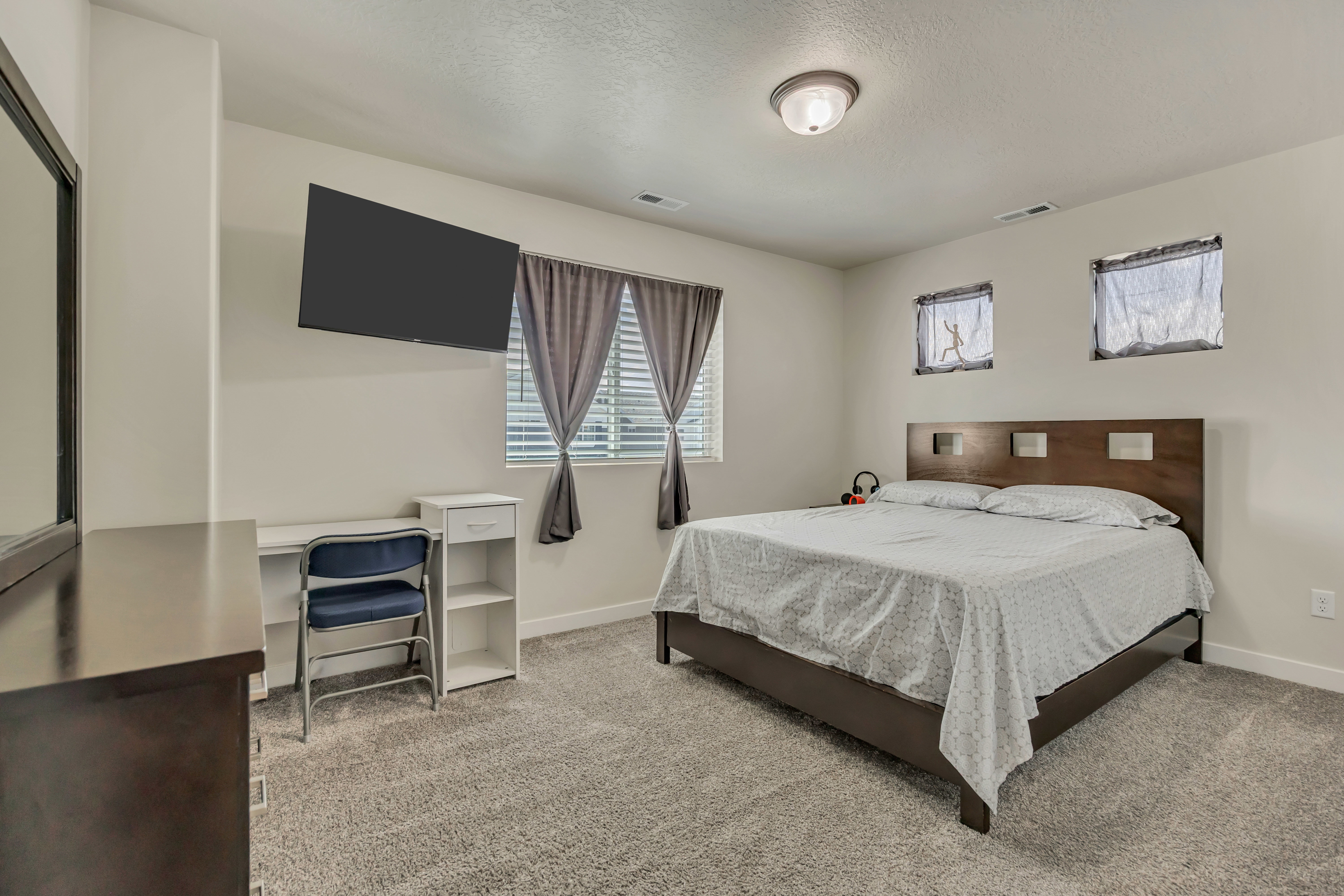 Carpeted room featuring multiple windows with blinds, a ceiling-mounted light fixture, and a wall-mounted television