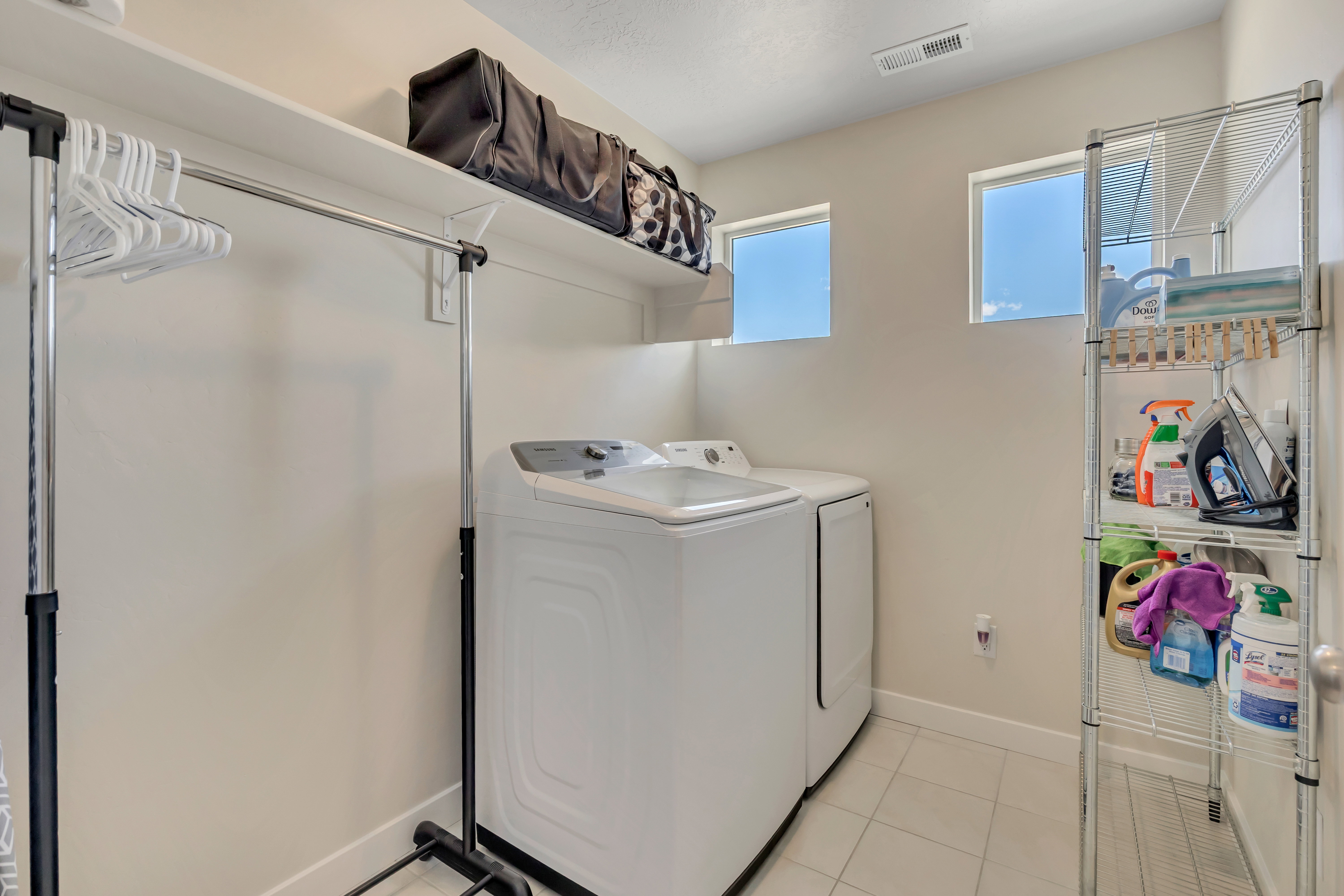 Laundry area featuring white tile flooring, upper shelving, and two windows providing natural light