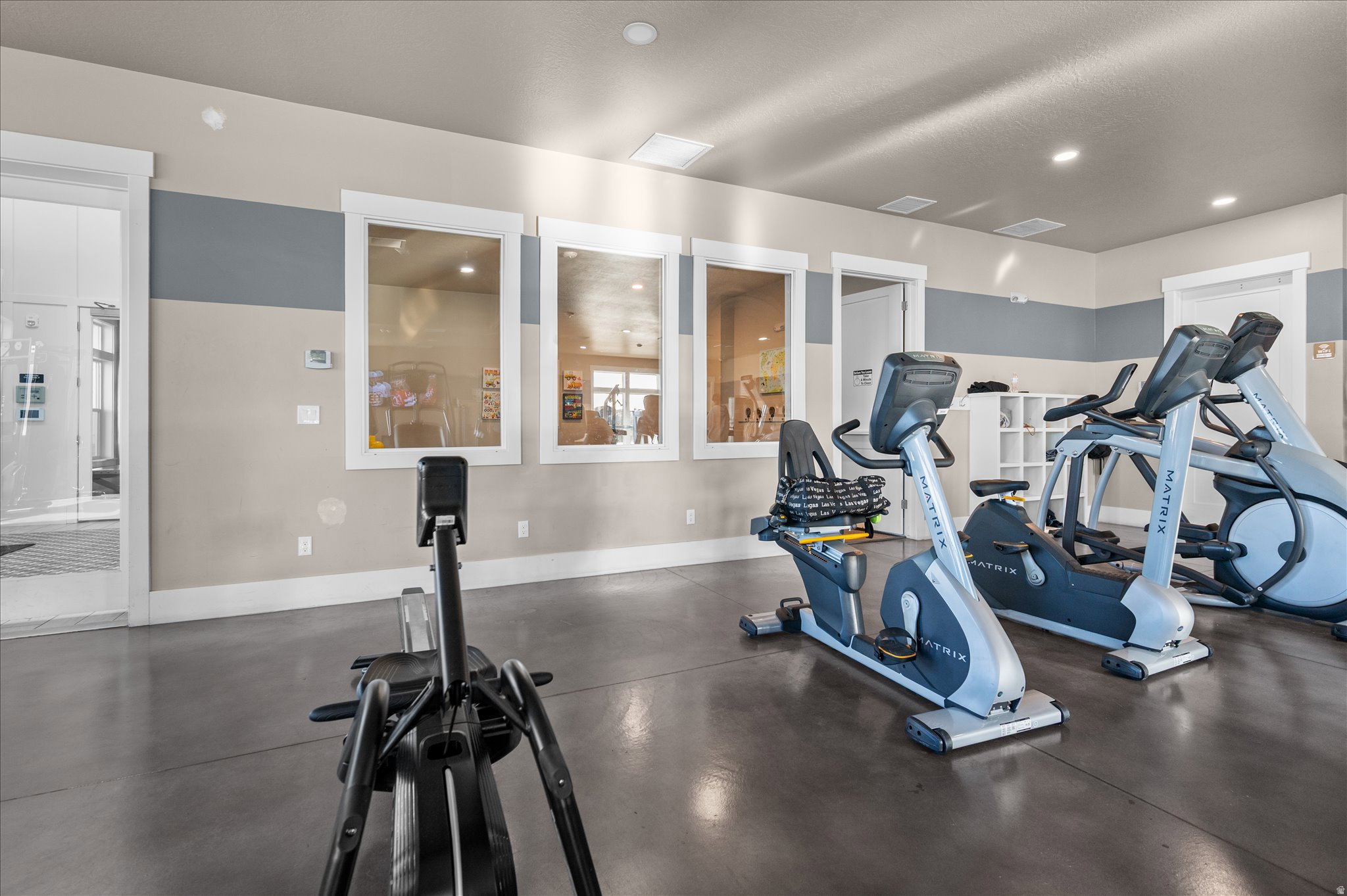 Recreational fitness area featuring smooth concrete flooring, a neutral two-tone painted wall, and multiple bright recessed ceiling lights