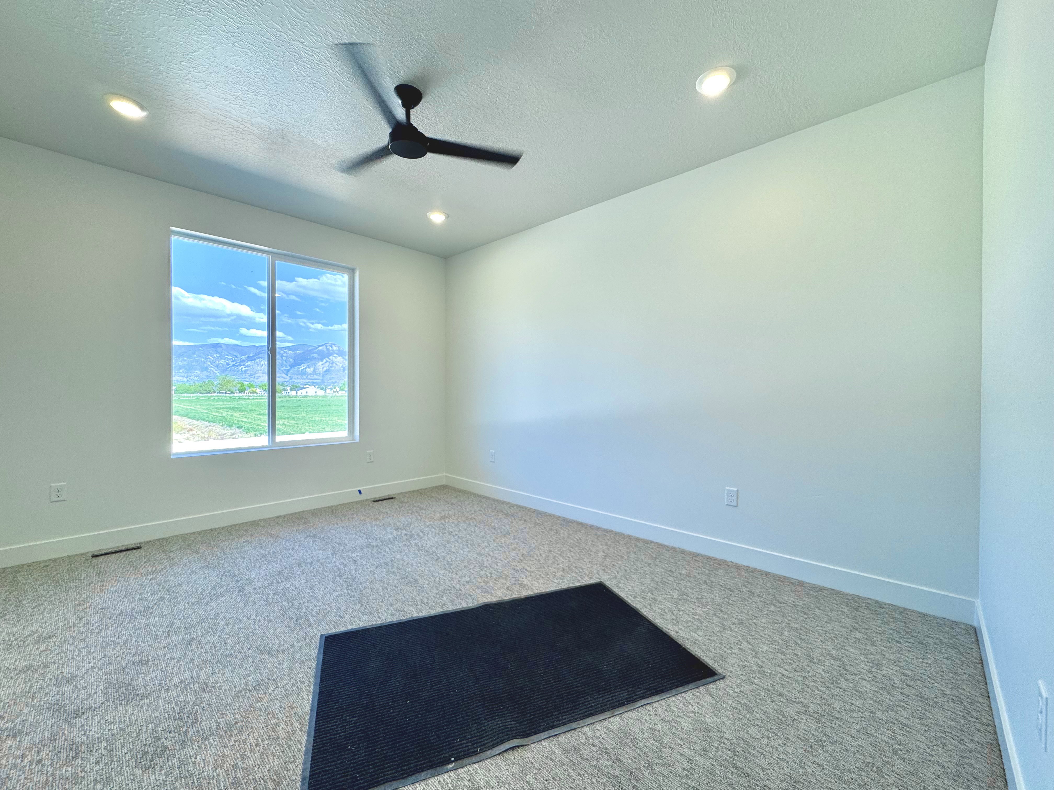 Spacious room featuring a large window, recessed lighting, ceiling fan, and light-colored carpeting