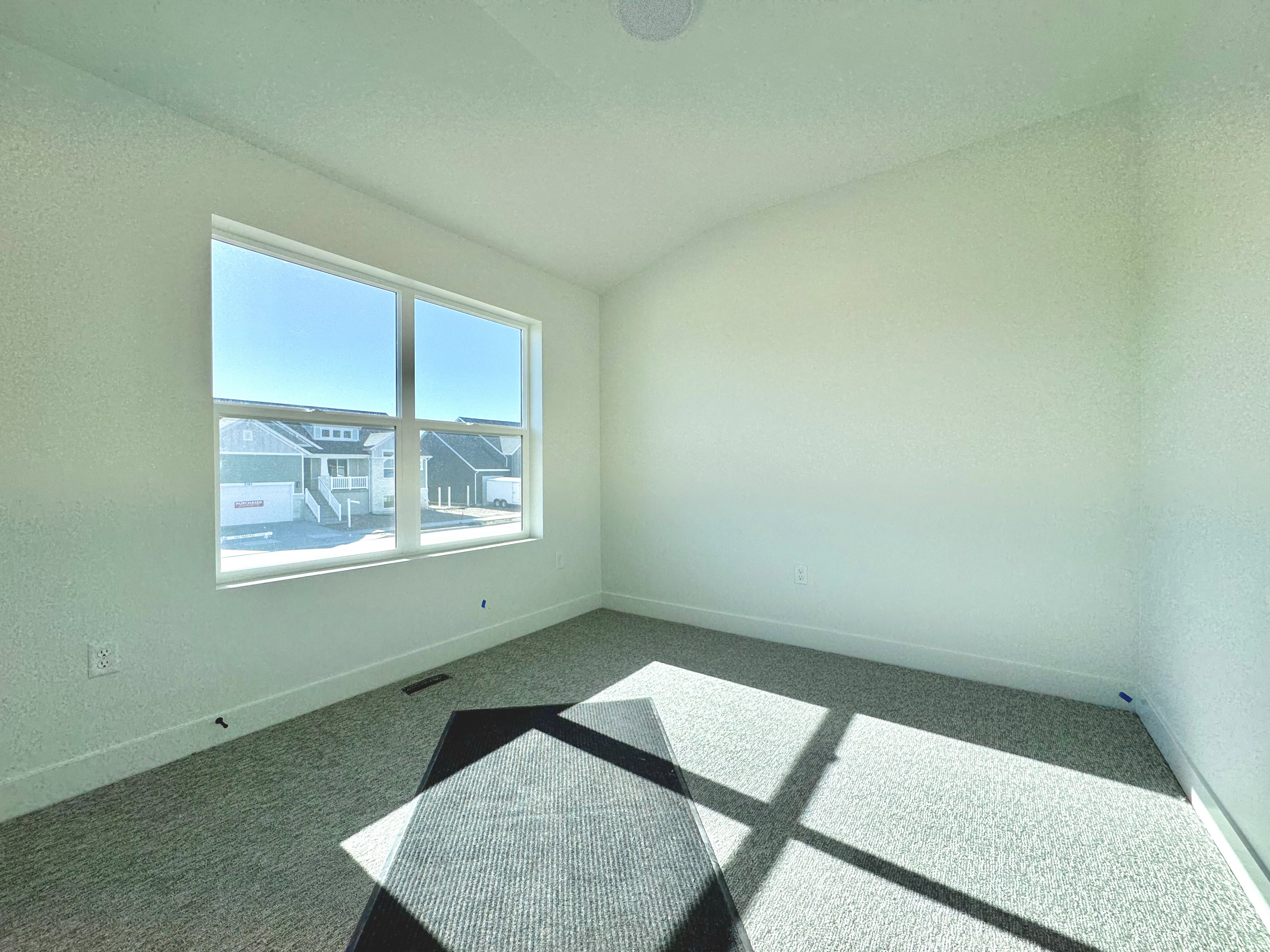 Bright interior room featuring a large window, light-colored carpet, white baseboards, and a recessed ceiling speaker