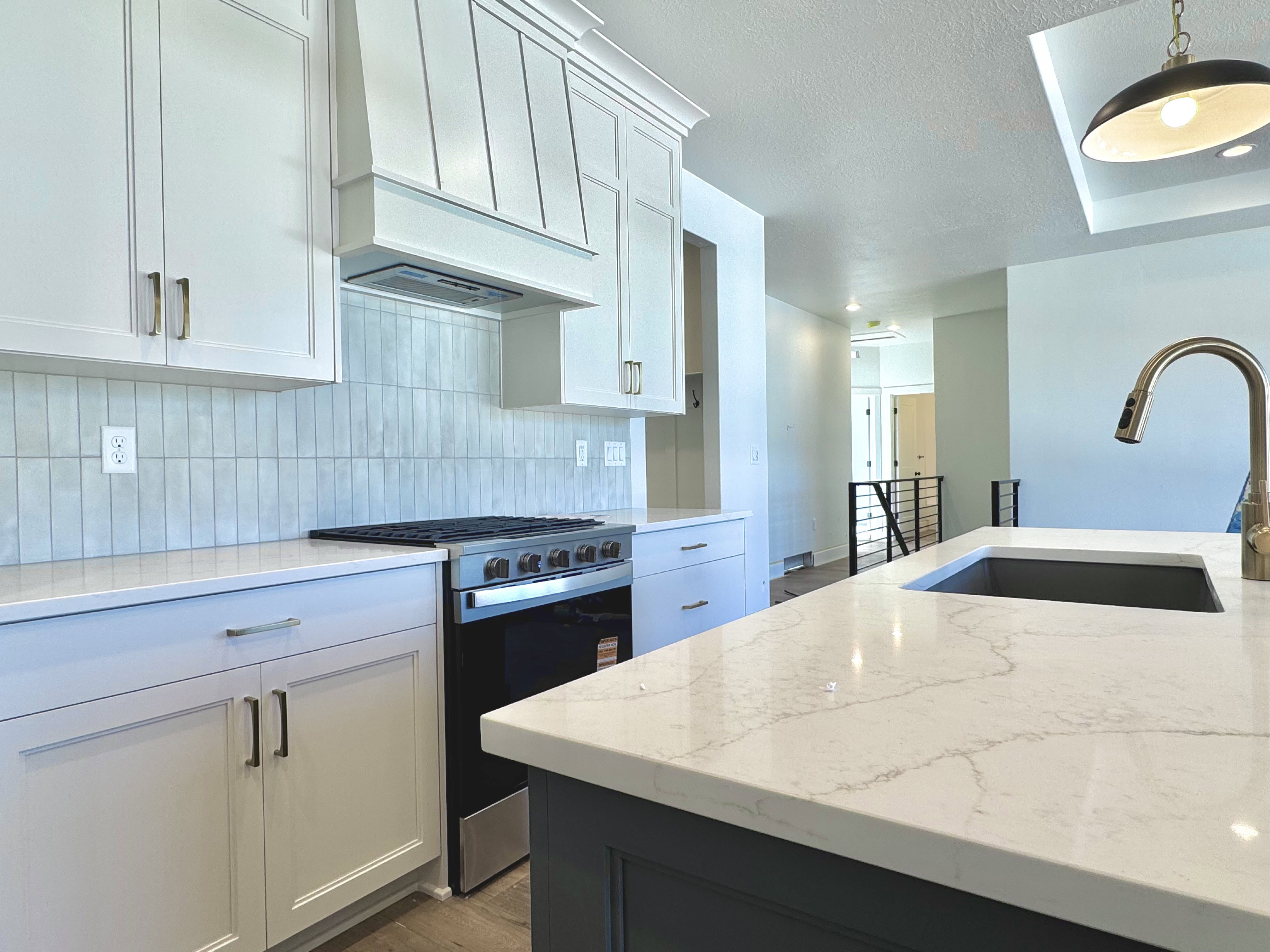 Modern kitchen featuring white shaker cabinetry and a large island with a composite stone countertop and integrated sink