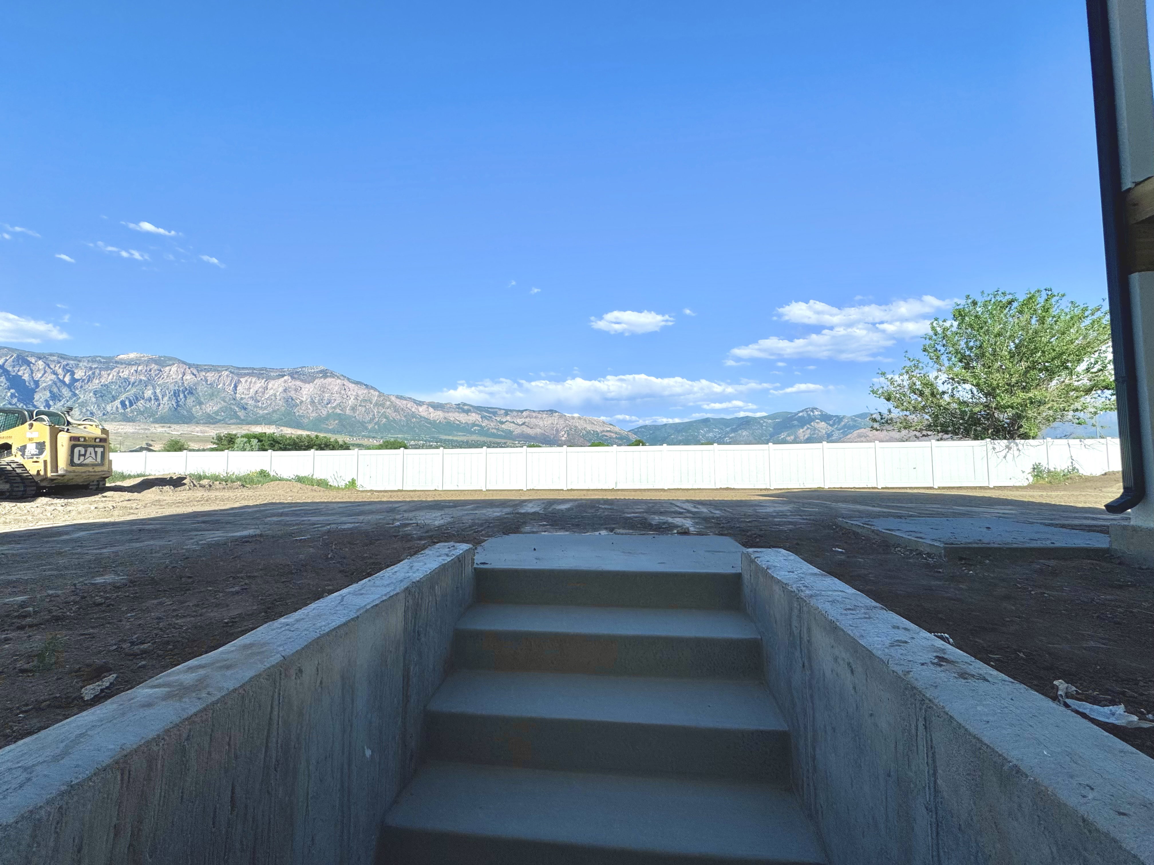 Concrete steps leading to a spacious, undeveloped lot with a white privacy fence