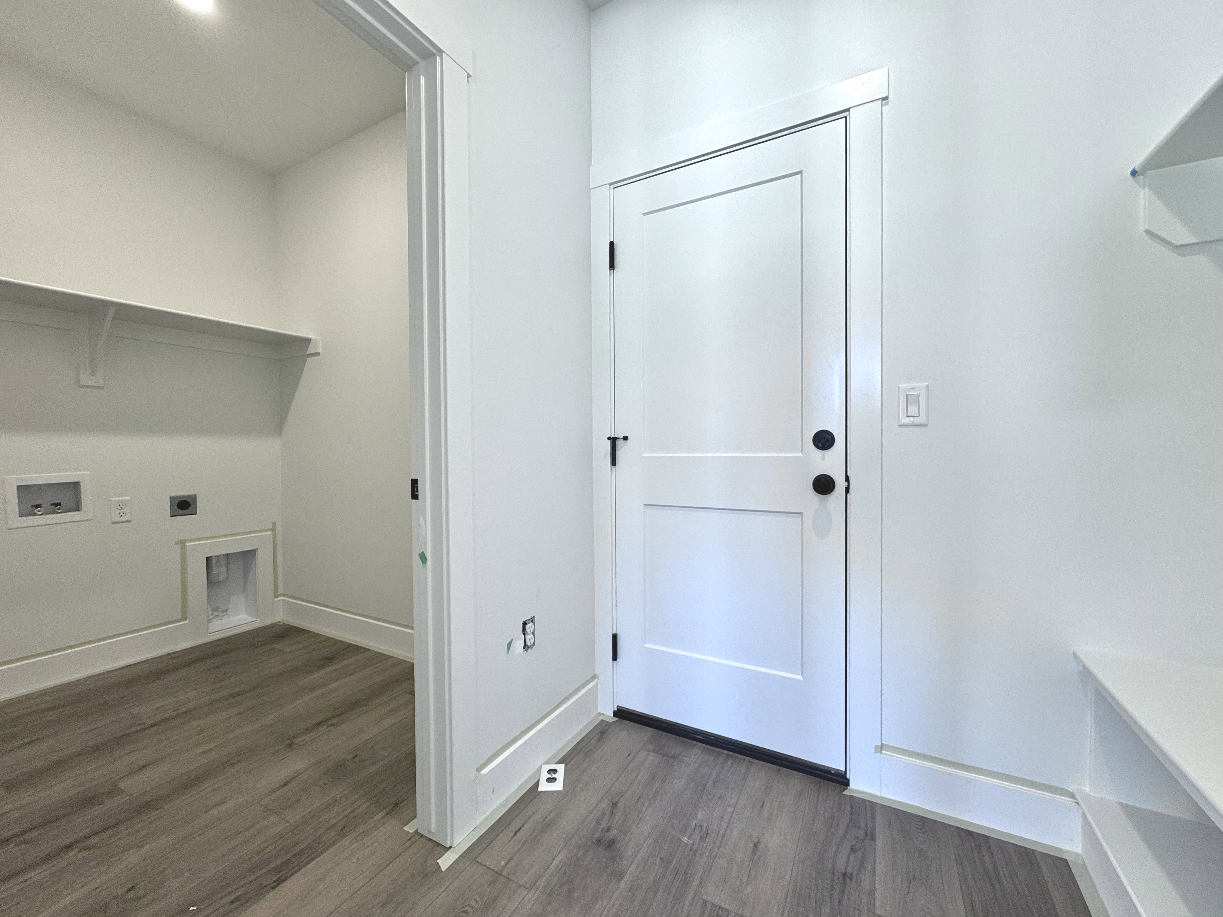 Mudroom entry featuring wood-finish flooring, crisp white walls, and a built-in bench with integrated shelving