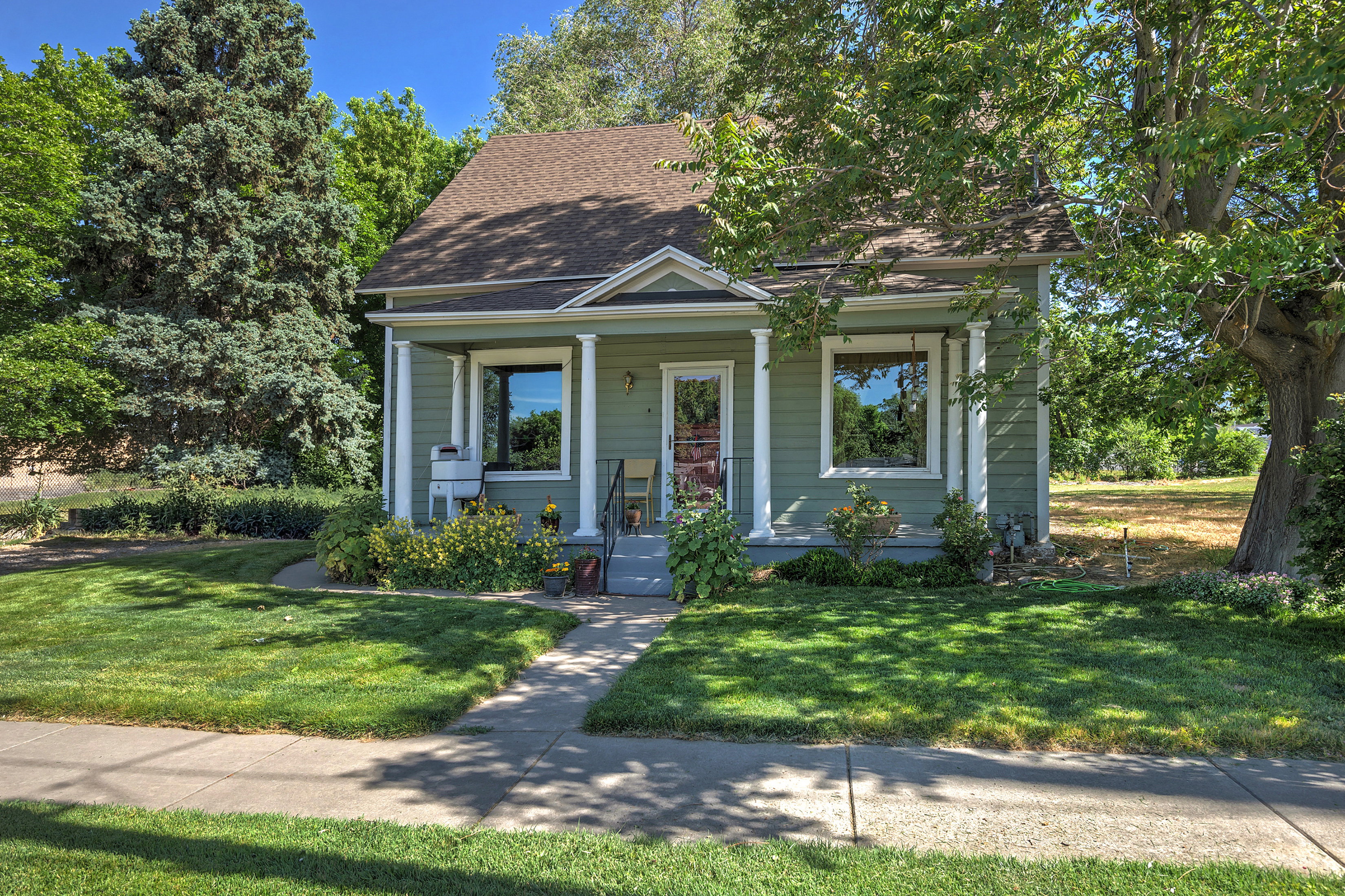 Charming single-story home featuring a covered front porch with white columns, a pitched roof, and light green siding