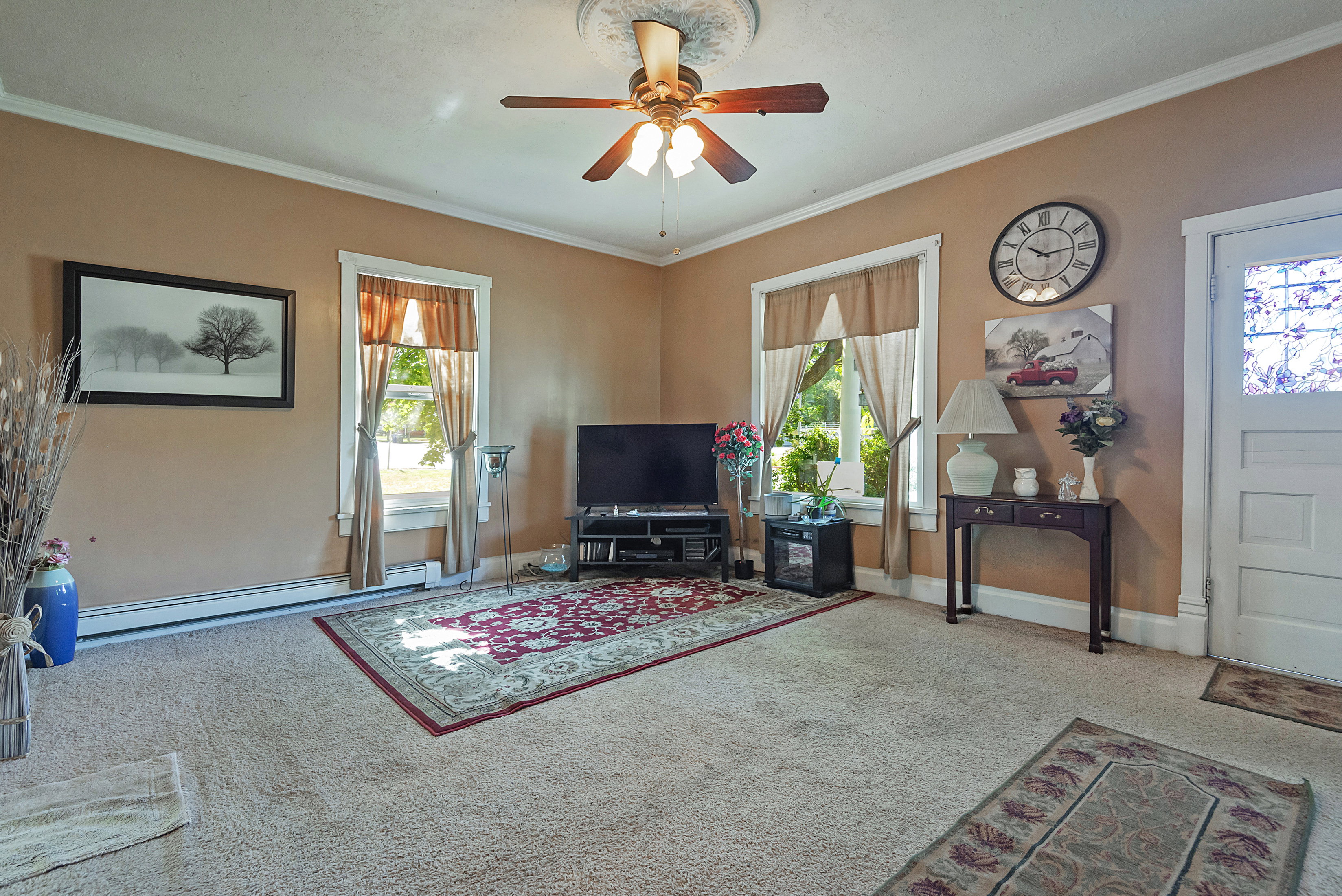 Interior living space featuring light-colored carpet, a ceiling fan with light fixture, and crown molding