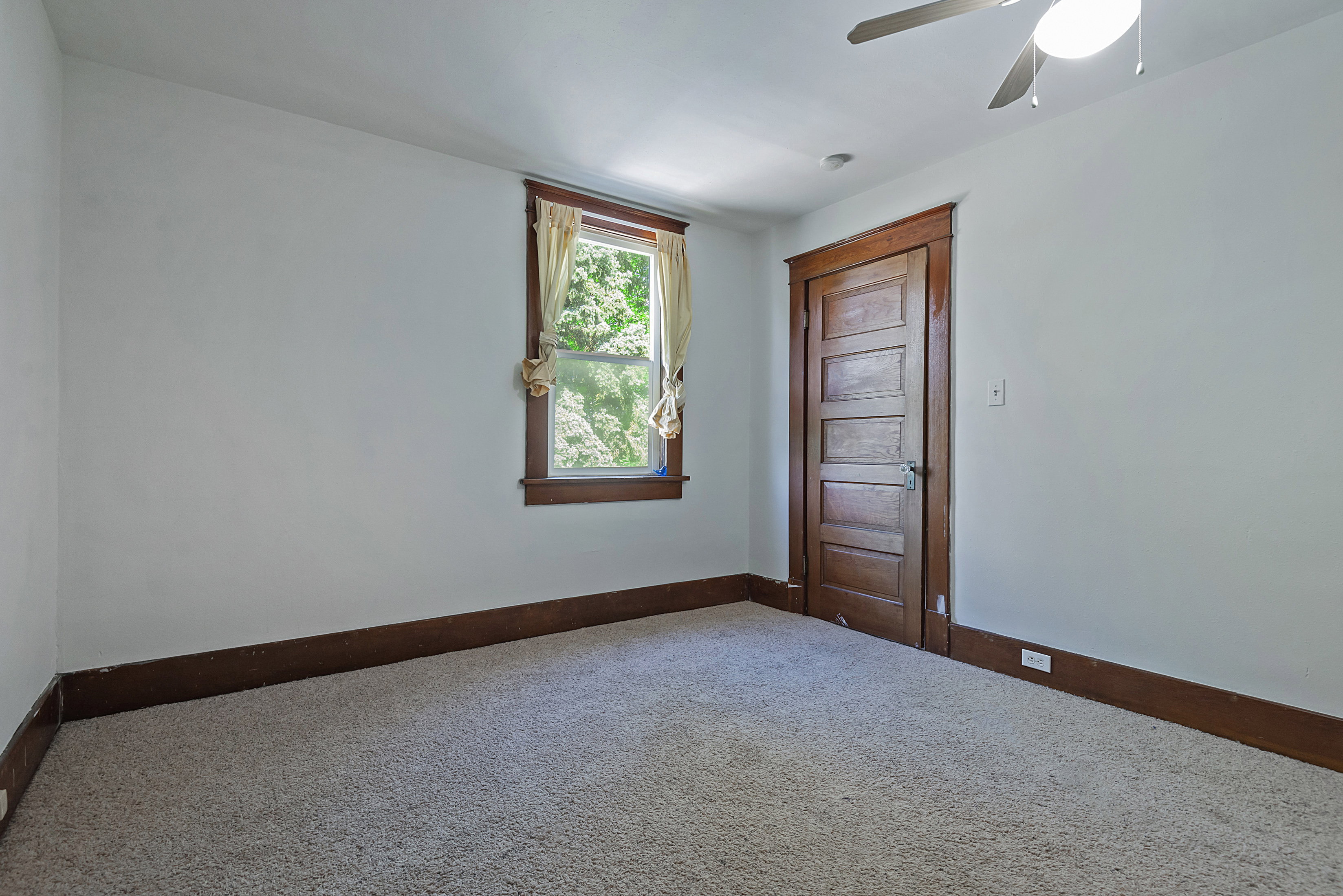 Carpeted room featuring a ceiling fan with light, a window with wood trim, and a paneled wood door with matching trim and baseboards