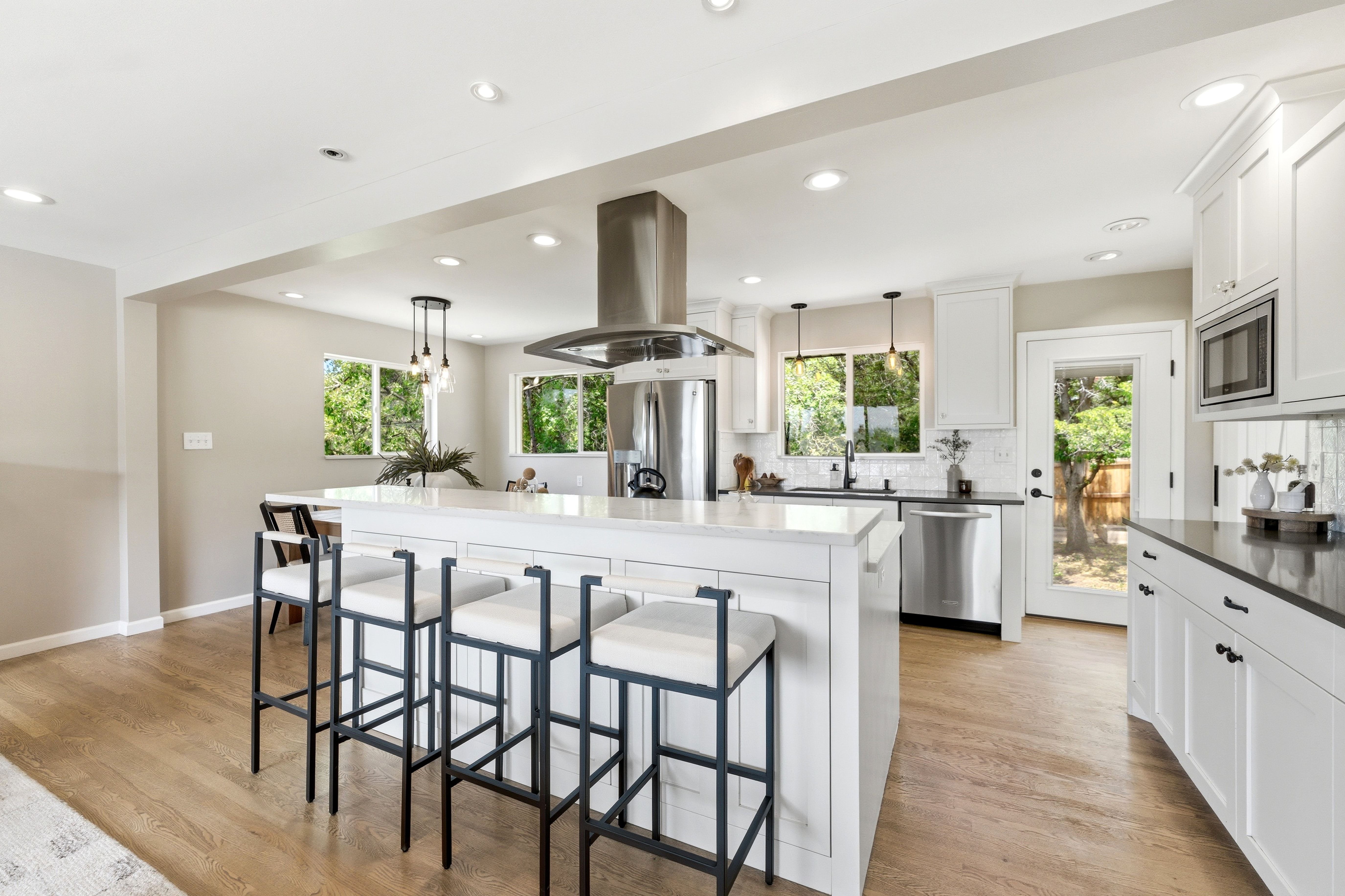 Kitchen featuring a large central island with seating, white shaker cabinetry, stainless steel appliances, and wood-finish flooring