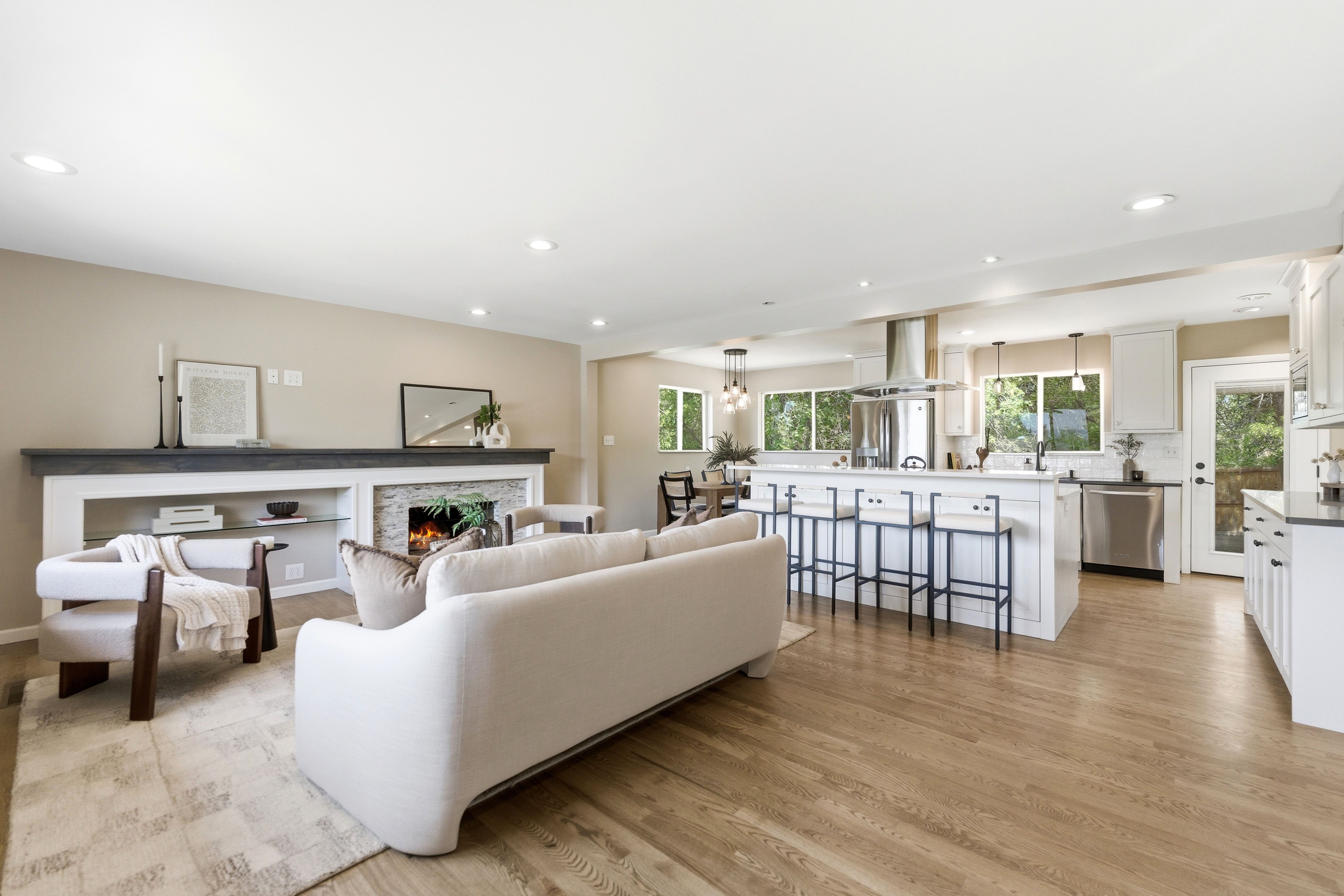 Open-concept living area featuring wood-finish flooring, a contemporary fireplace with stone surround, a kitchen island with seating, white cabinetry, and stainless steel appliances
