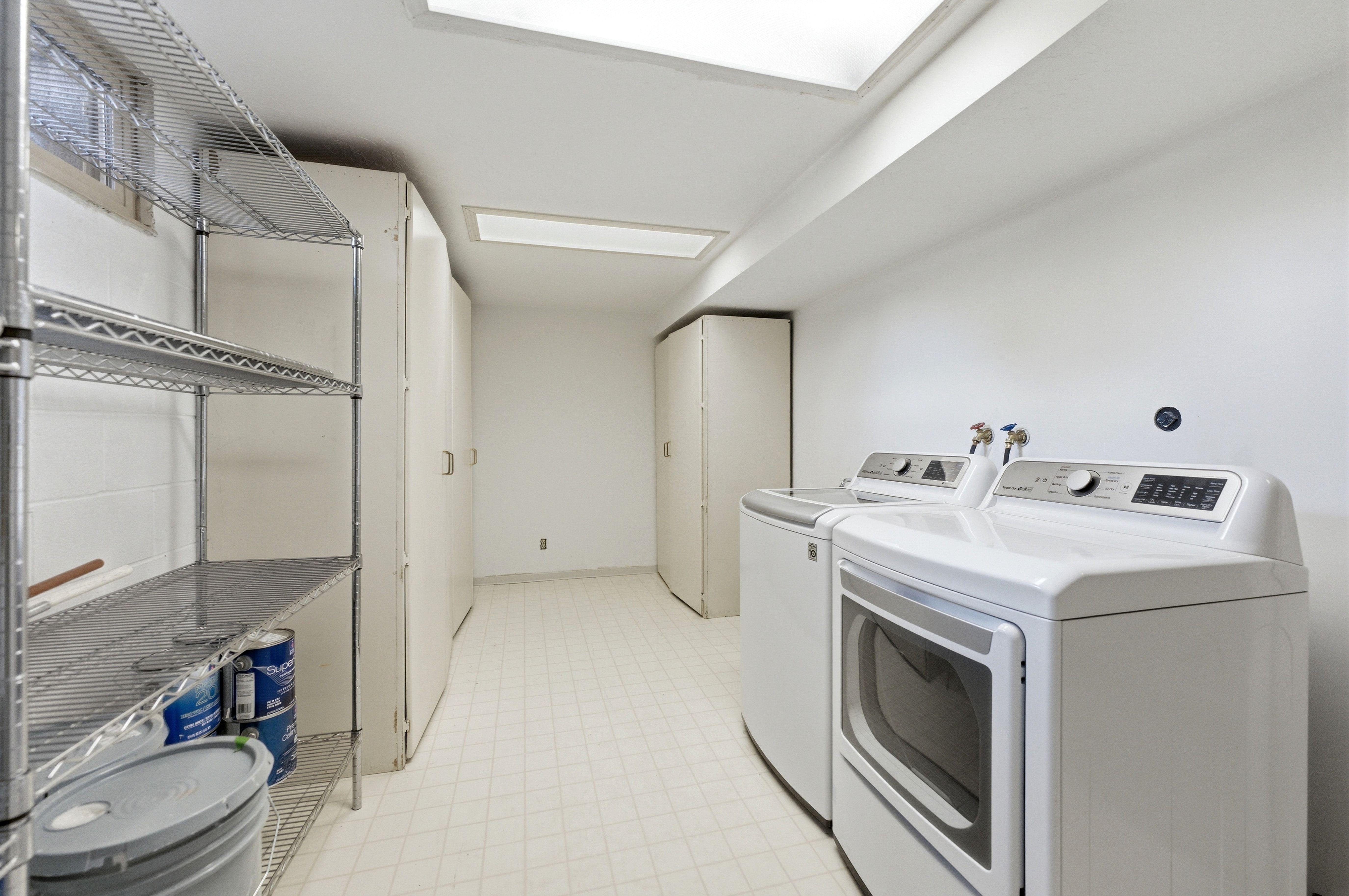 Dedicated laundry area featuring white appliances, ample built-in storage cabinetry, resilient flooring, and overhead fluorescent lighting