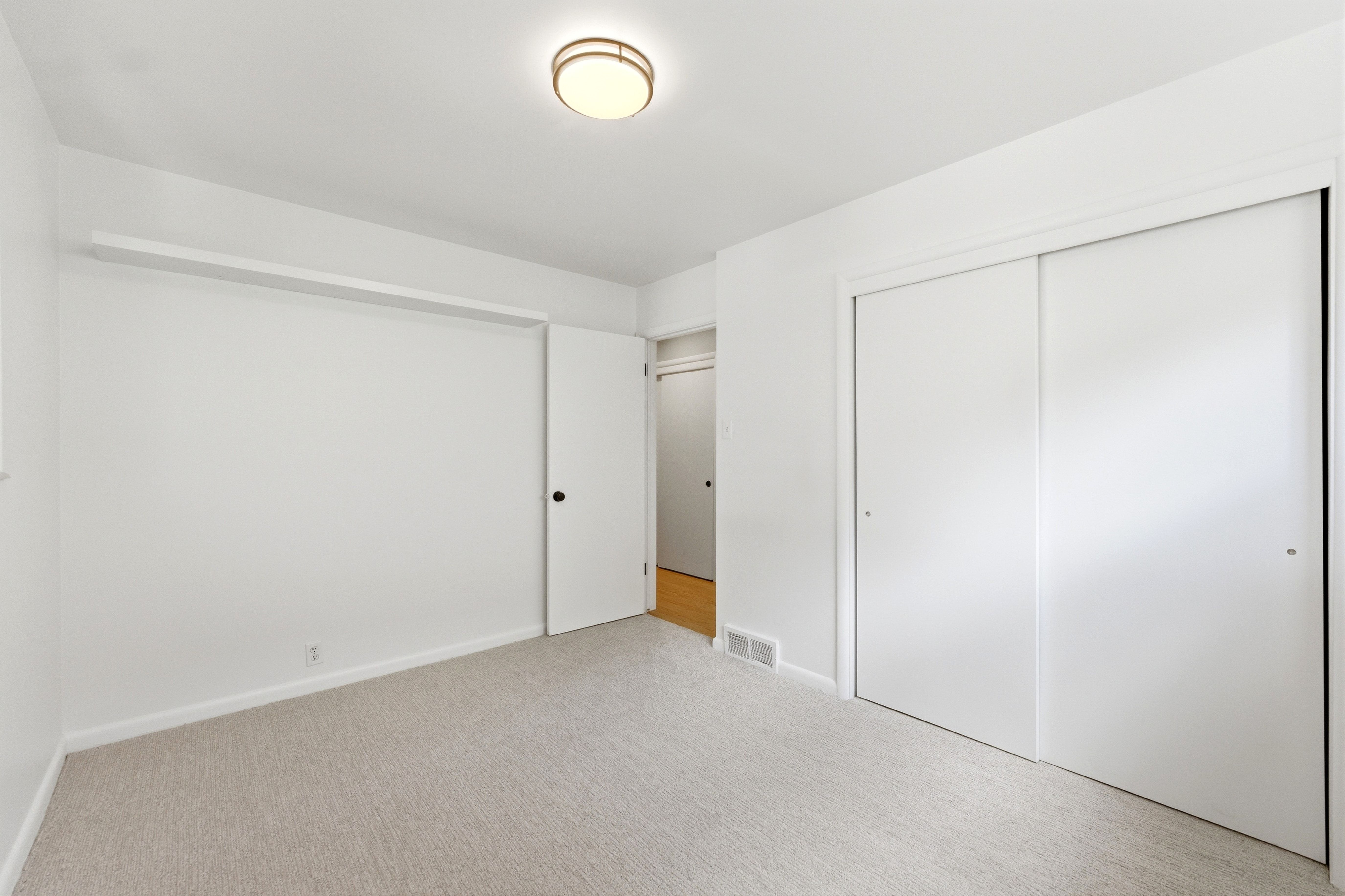 Carpeted room with white walls, a flush-mount ceiling light fixture, and a built-in closet with sliding doors