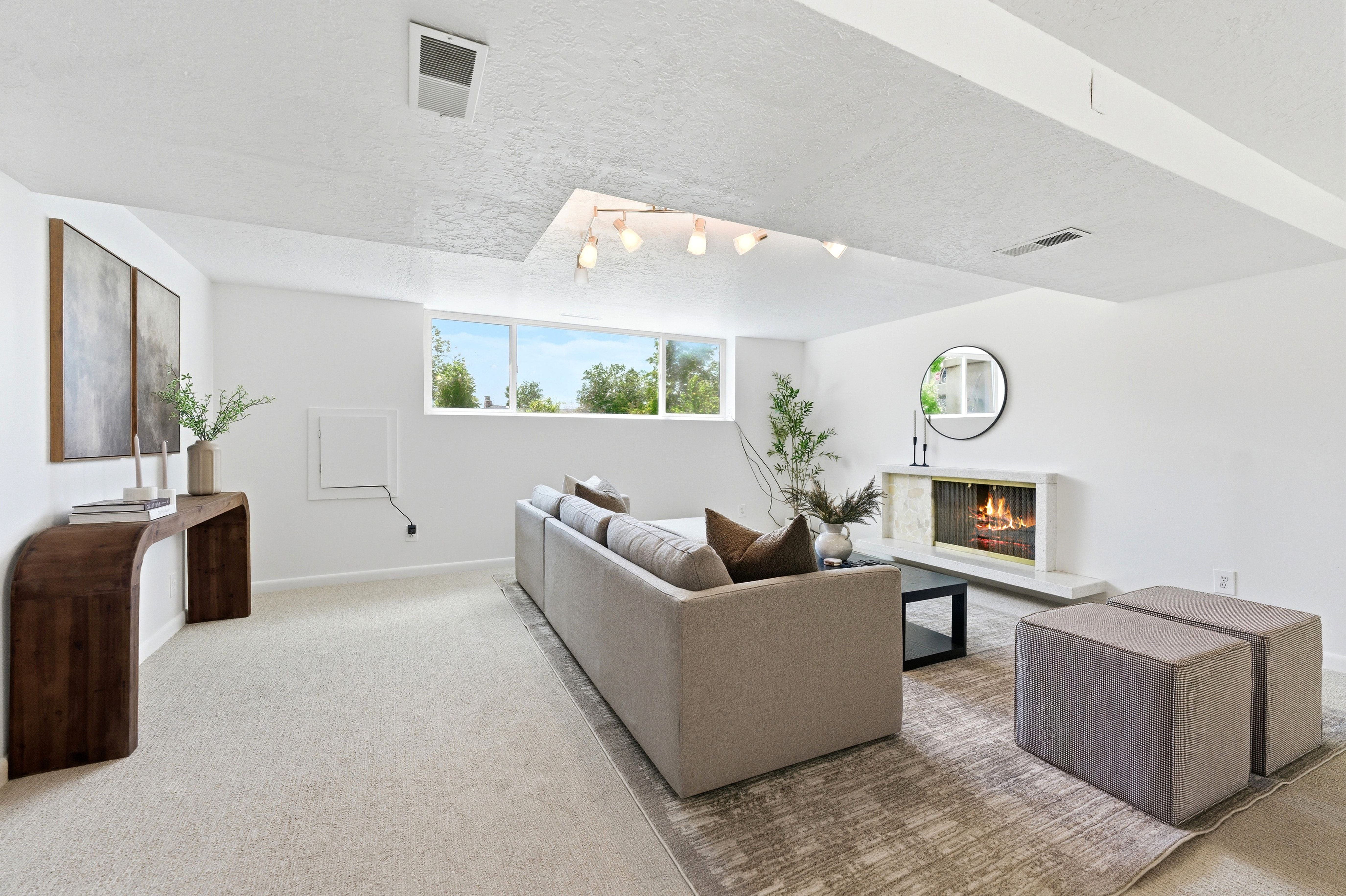 Spacious room featuring a fireplace with a light-toned surround, a built-in linear light fixture, a window providing natural light, and light-colored carpeting