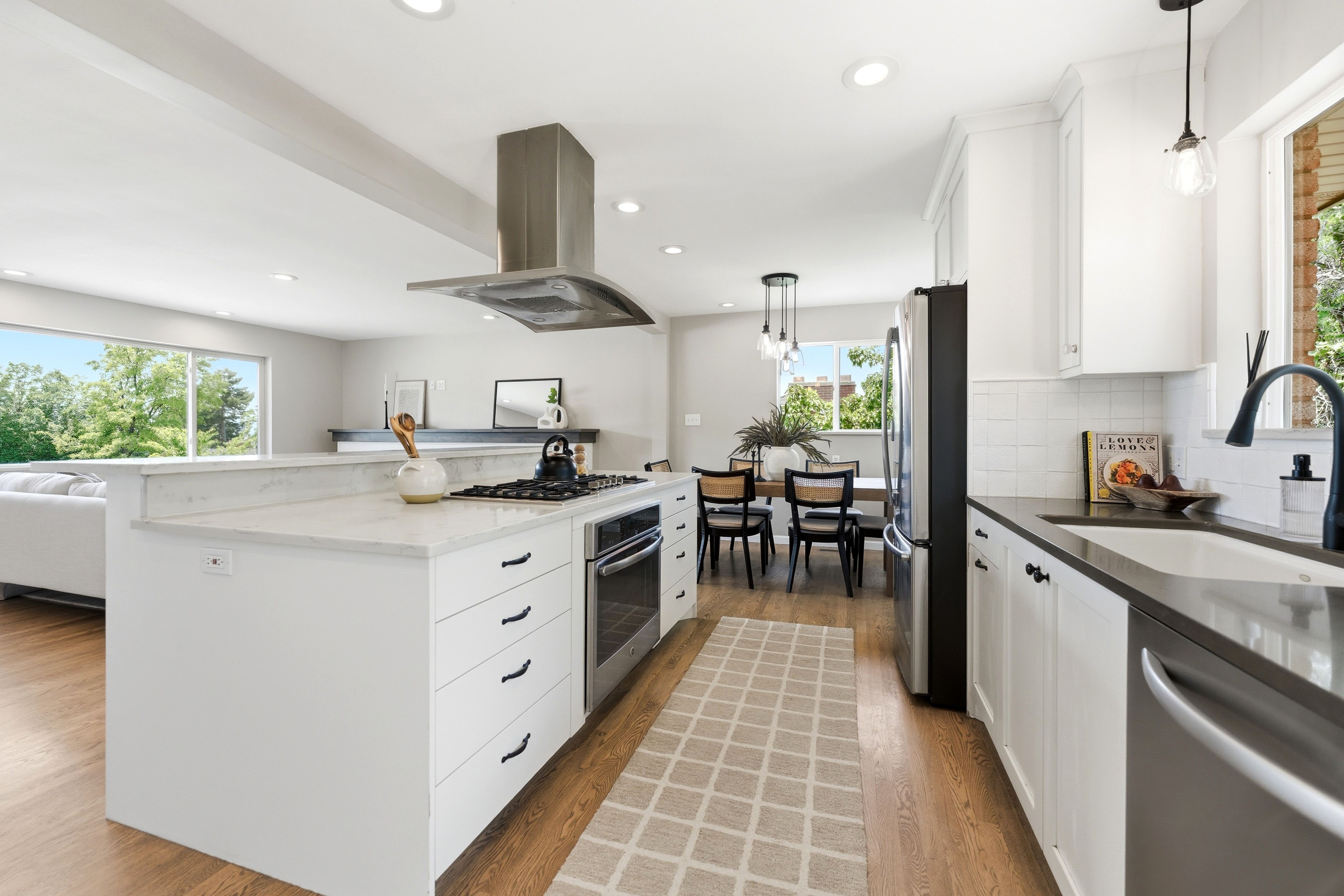 Modern kitchen featuring white cabinetry, a large center island with a built-in range, stainless steel appliances, and wood-finish flooring
