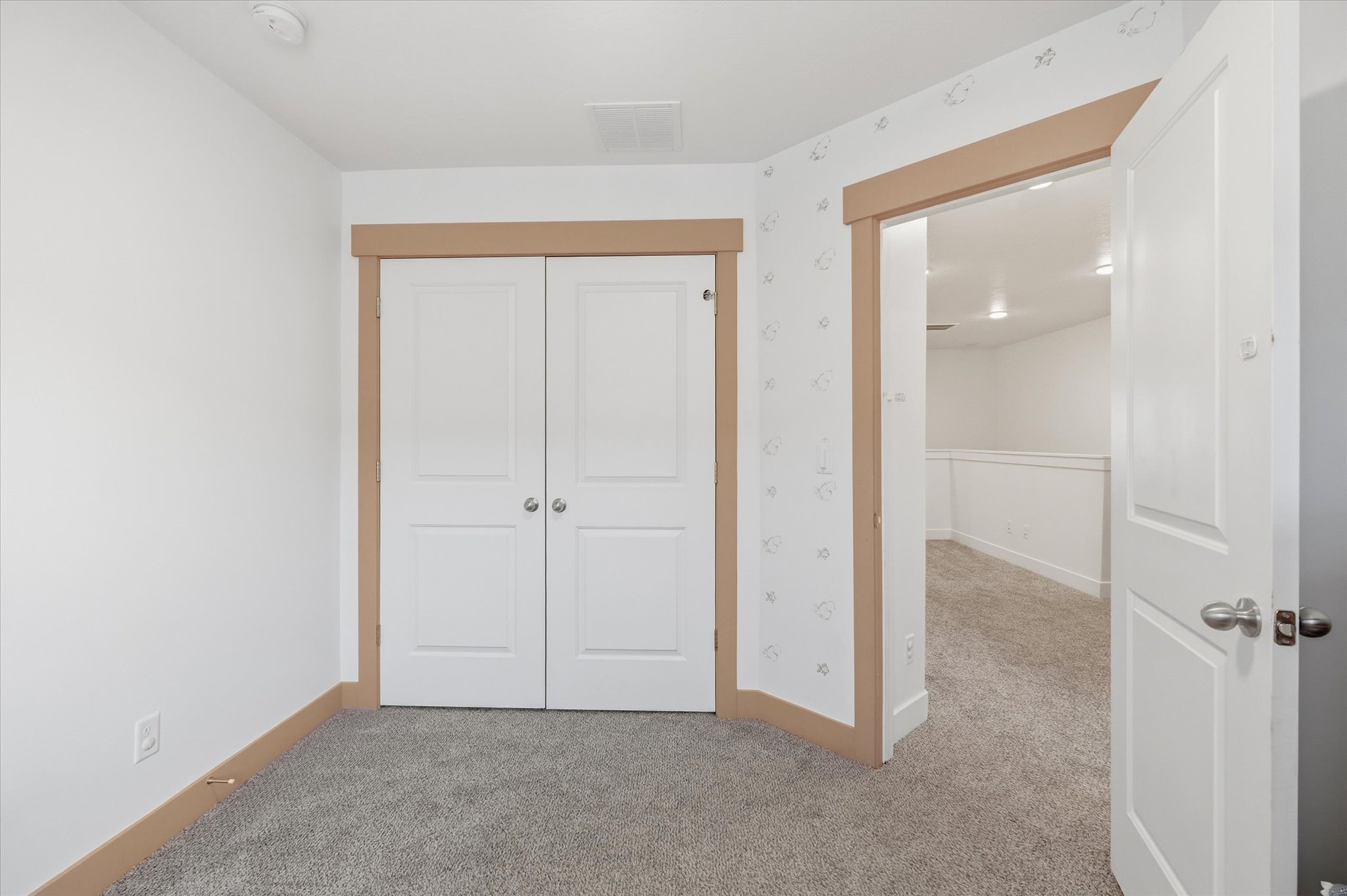 Carpeted room featuring white walls, a built-in double-door closet with panel detailing, and natural wood-finish trim