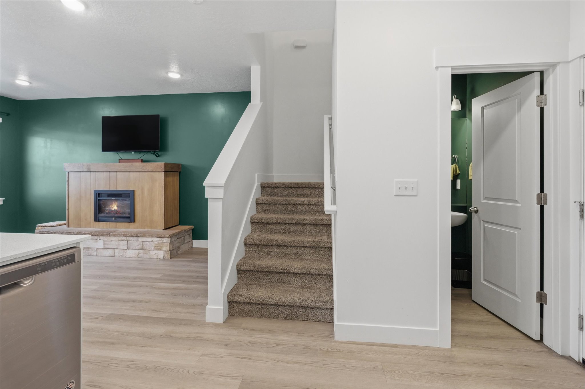 Carpeted staircase with white balustrade, wood-finish flooring, and a fireplace featuring a stone base and wood-finish surround