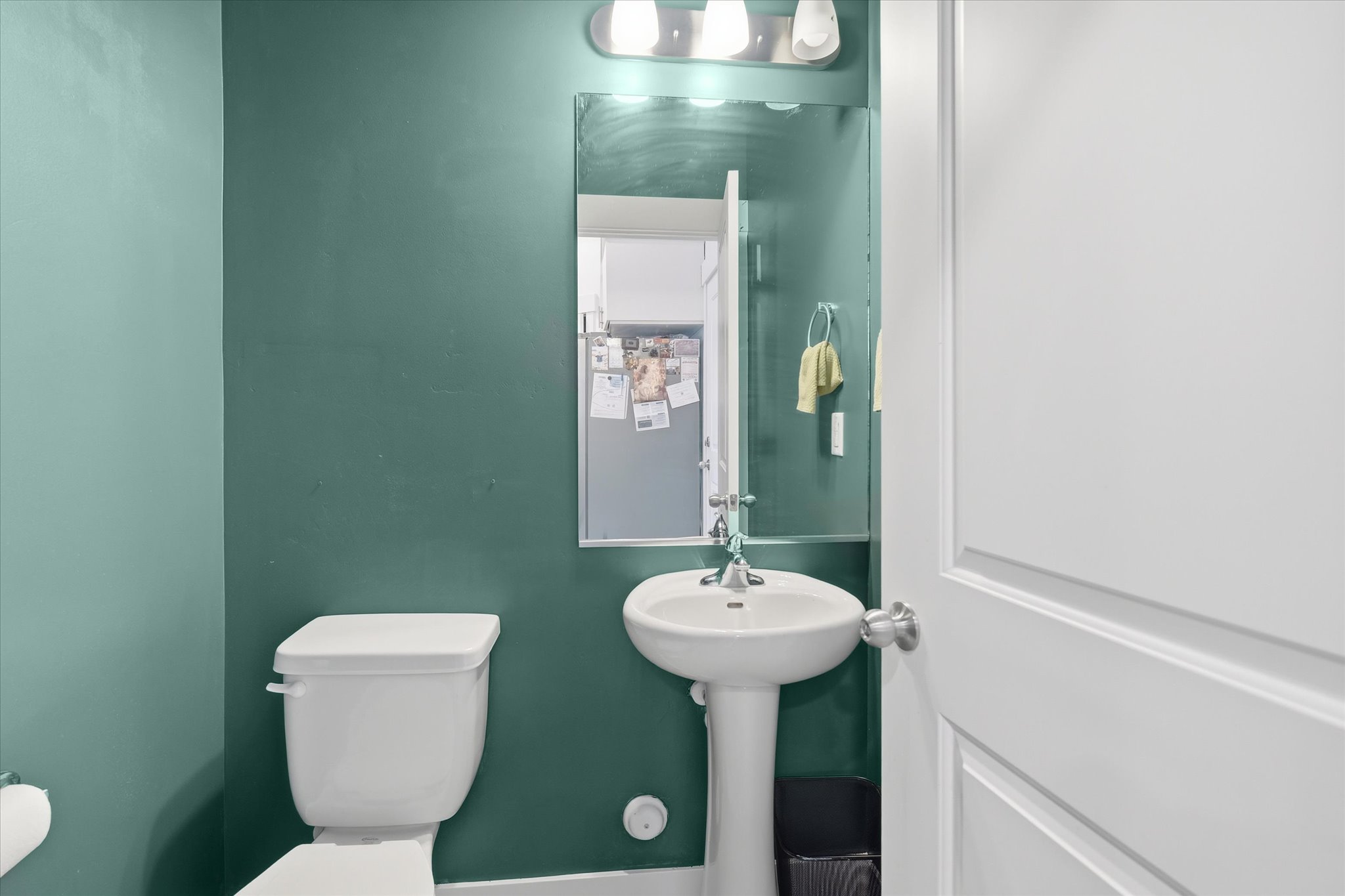 Pedestal sink with chrome fixtures, framed mirror, and three-light vanity bar
