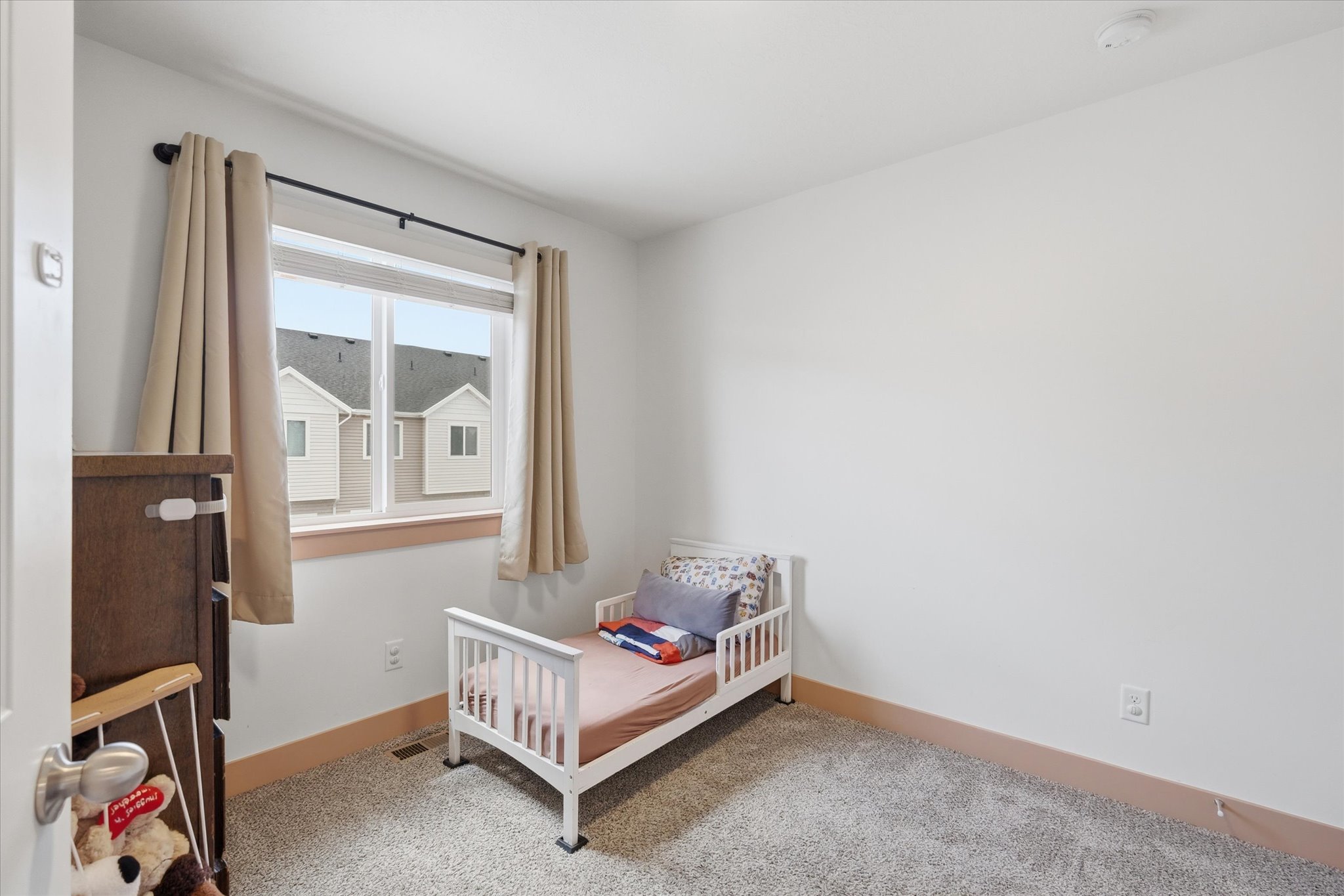 Spacious room featuring light gray carpet, white walls, and a large window with natural wood trim