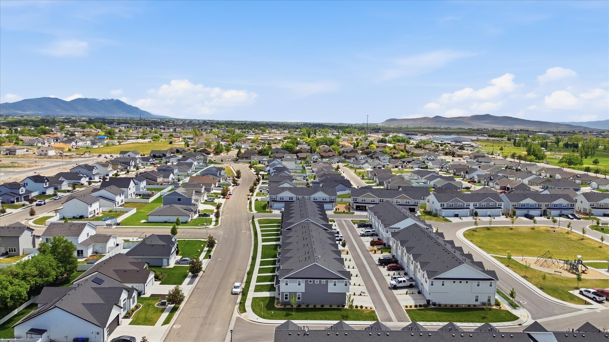 Expansive residential development featuring a variety of housing types, broad paved streets, and a clear mountain backdrop